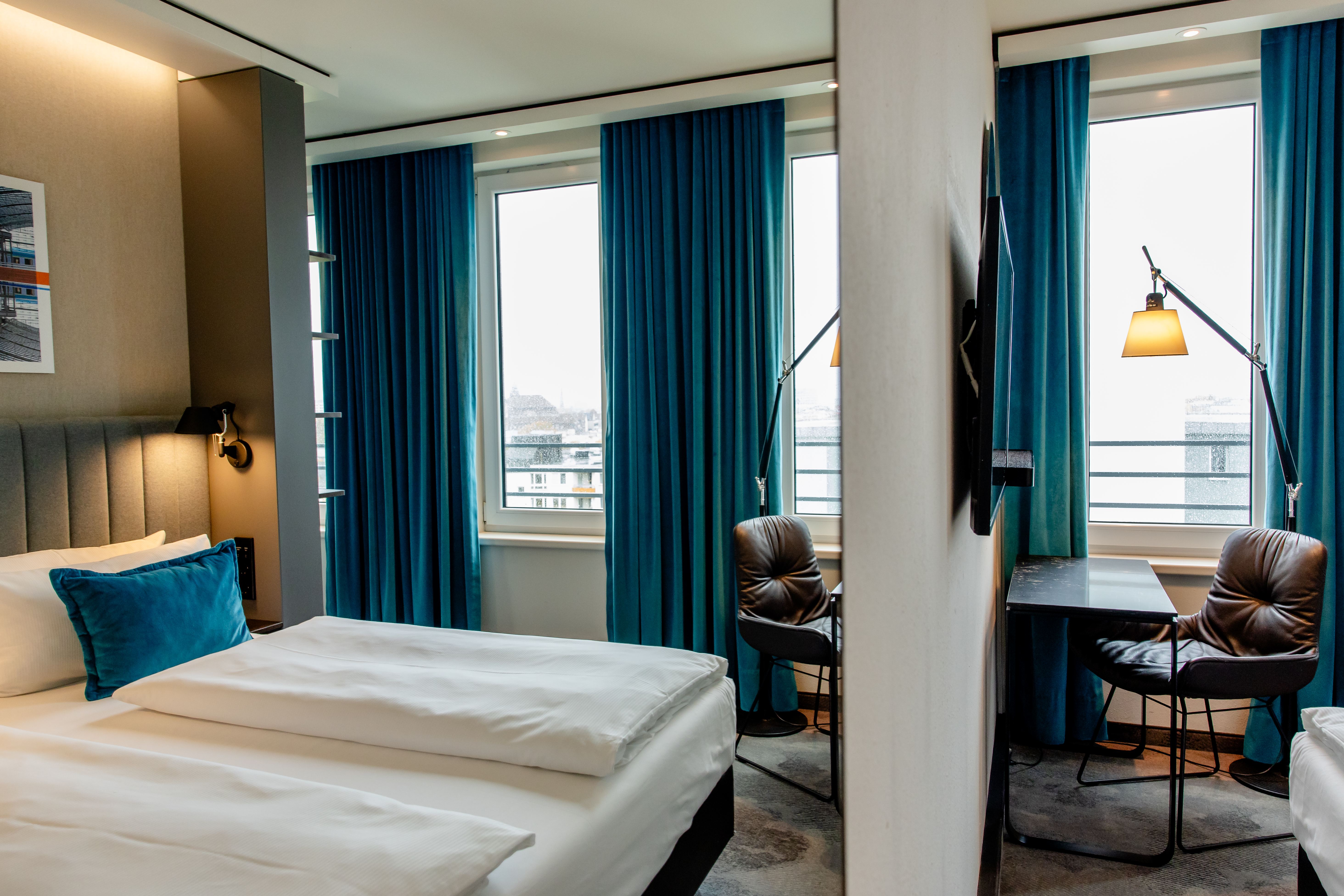 Hotel Motel One Berlin-Hauptbahnhof Modern eingerichtetes Hotelzimmer mit gemütlichem Doppelbett, großen Fenstern und blauem Vorhang. Arbeitsbereich mit Lederstuhl und Schreibtisch, angenehmes Licht und ruhige Atmosphäre für Erholung und produktives Arbeiten. Hotel Motel One Berlin-Hauptbahnhof Modern eingerichtetes Hotelzimmer mit gemütlichem Doppelbett, großen Fenstern und blauem Vorhang. Arbeitsbereich mit Lederstuhl und Schreibtisch, angenehmes Licht und ruhige Atmosphäre für Erholung und produktives Arbeiten.