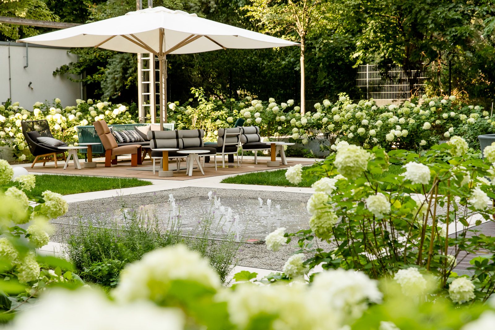 hotel Berlin Hauptbahnhof Motel One outdoor area with stylish lounge furniture, large parasol, water feature, and blooming white hydrangeas