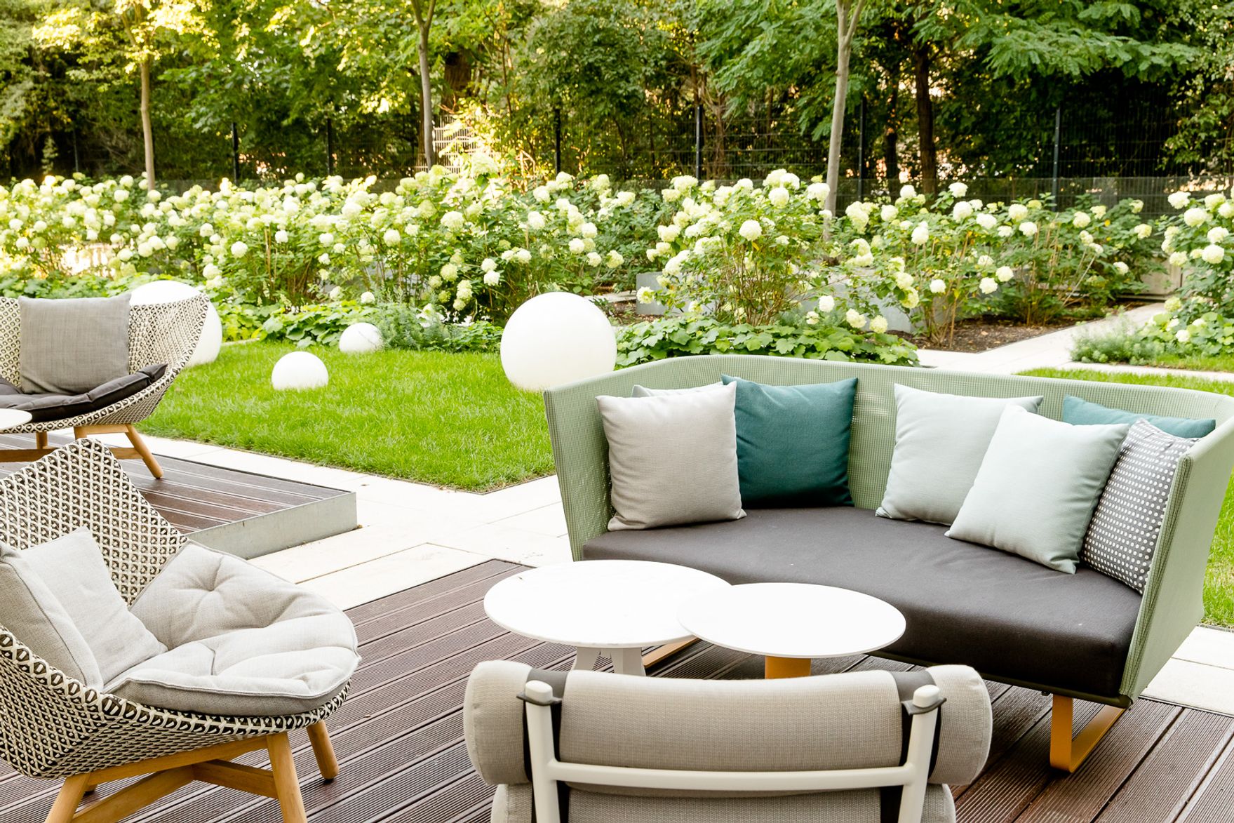 Hotel Berlin Hauptbahnhof Motel One gemütlicher Außenbereich mit Loungemöbeln in einem Garten, umgeben von Hortensien