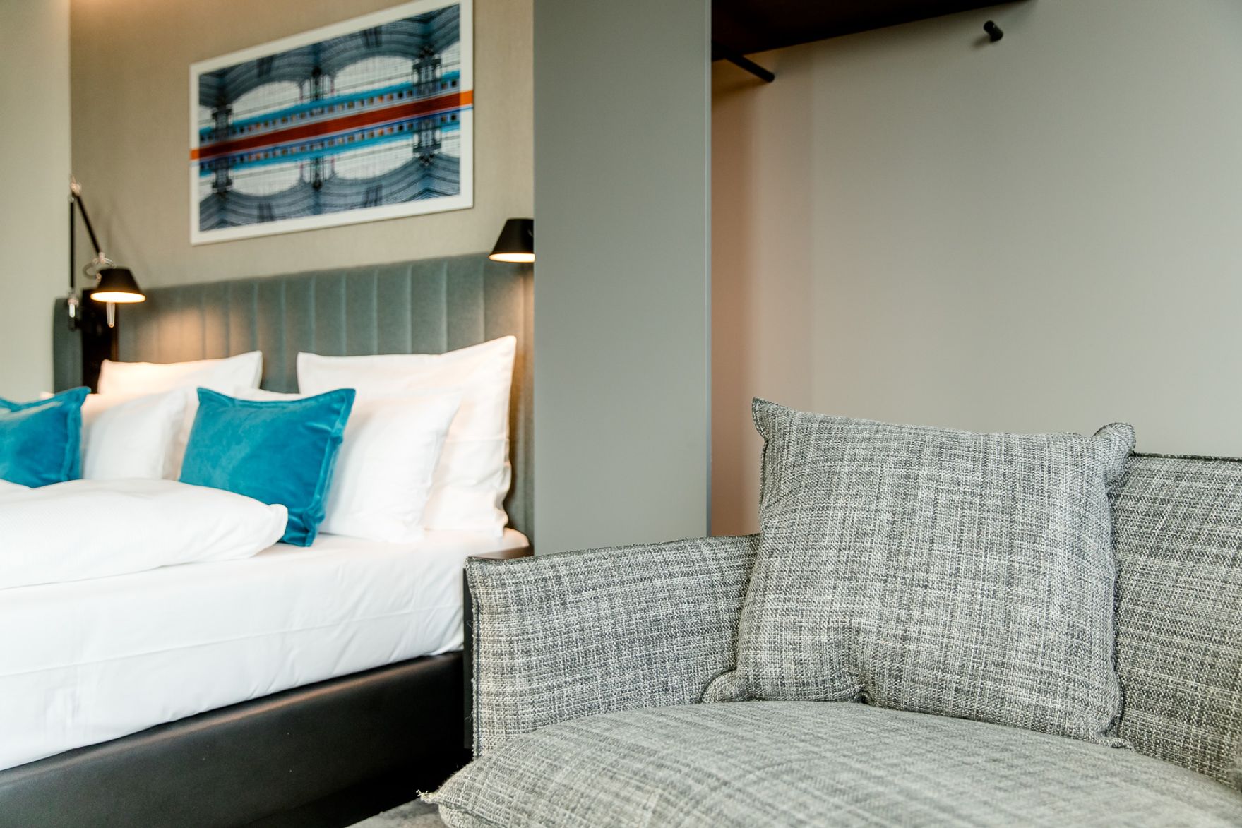 Hotel Berlin Hauptbahnhof Motel One helles Zimmer mit Blick auf ein Sofa sowie ein Doppelbett mit zwei Zierkissen in türkis