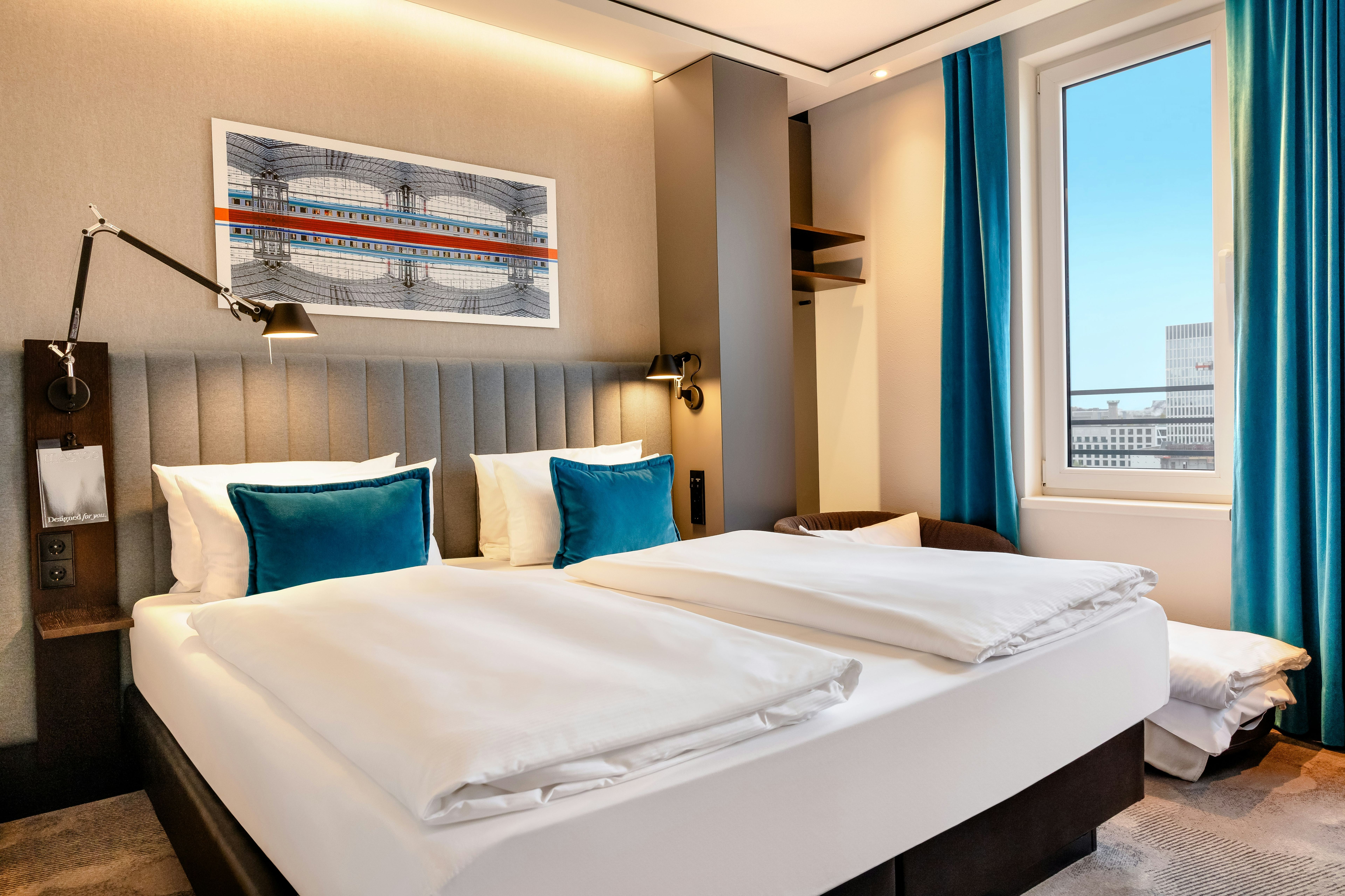 Hotel Motel One Berlin-Hauptbahnhof Modern eingerichtetes Hotelzimmer mit großem Doppelbett, hellen Wänden, blauen Akzentkissen und Vorhängen sowie großem Fenster mit Stadtblick. Hotel Motel One Berlin-Hauptbahnhof Modern eingerichtetes Hotelzimmer mit großem Doppelbett, hellen Wänden, blauen Akzentkissen und Vorhängen sowie großem Fenster mit Stadtblick.