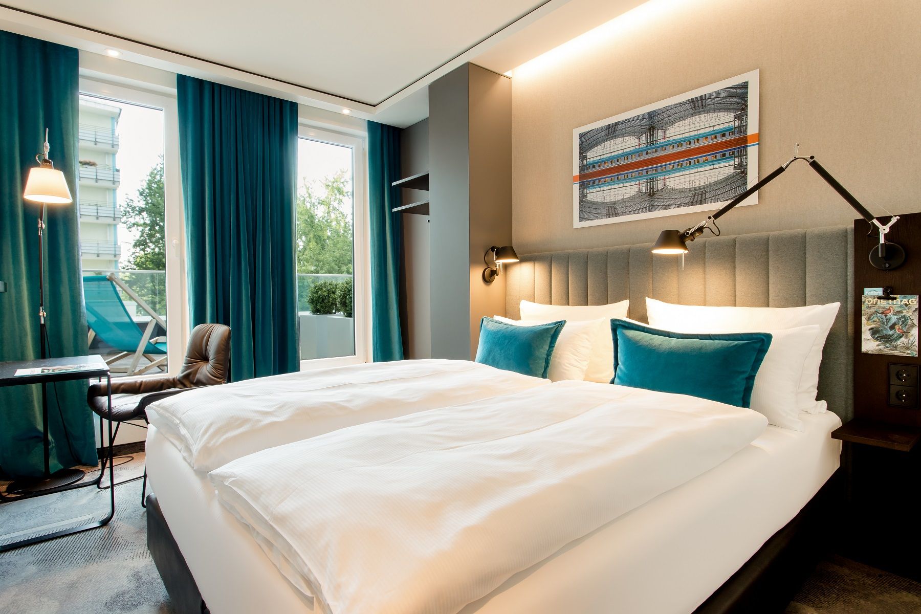 Designhotel Berlin Hauptbahnhof Motel One lichtdurchflutetes Balkonzimmer mit Doppelbett, Tisch und Stuhl sowie Blick auf einen Liegestuhl auf dem Balkon