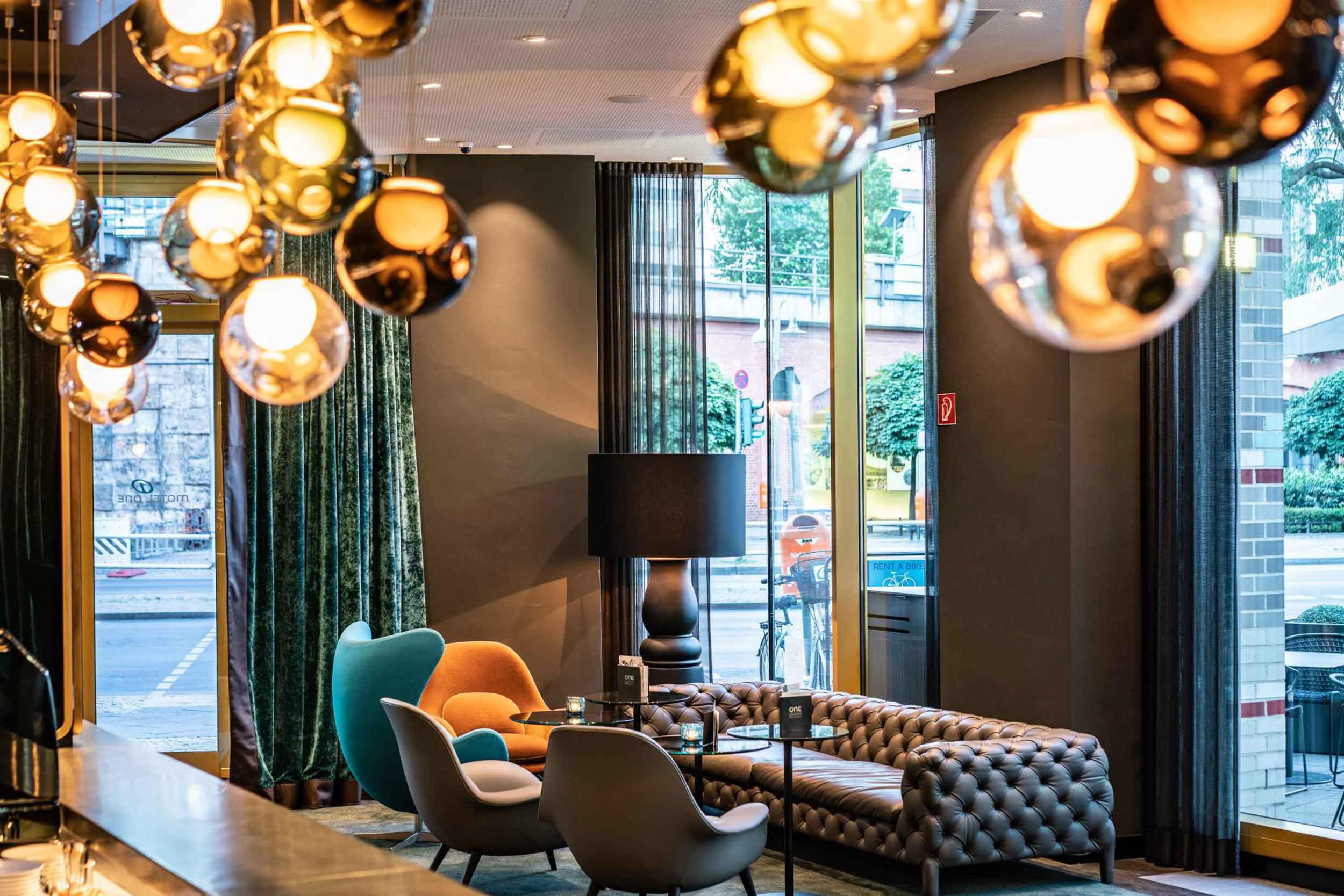 Hotel Berlin Ku’damm Motel One Lounge mit bodentiefen Fenstern und einer Sitzgruppe, bestehend aus Sofa und Sesseln