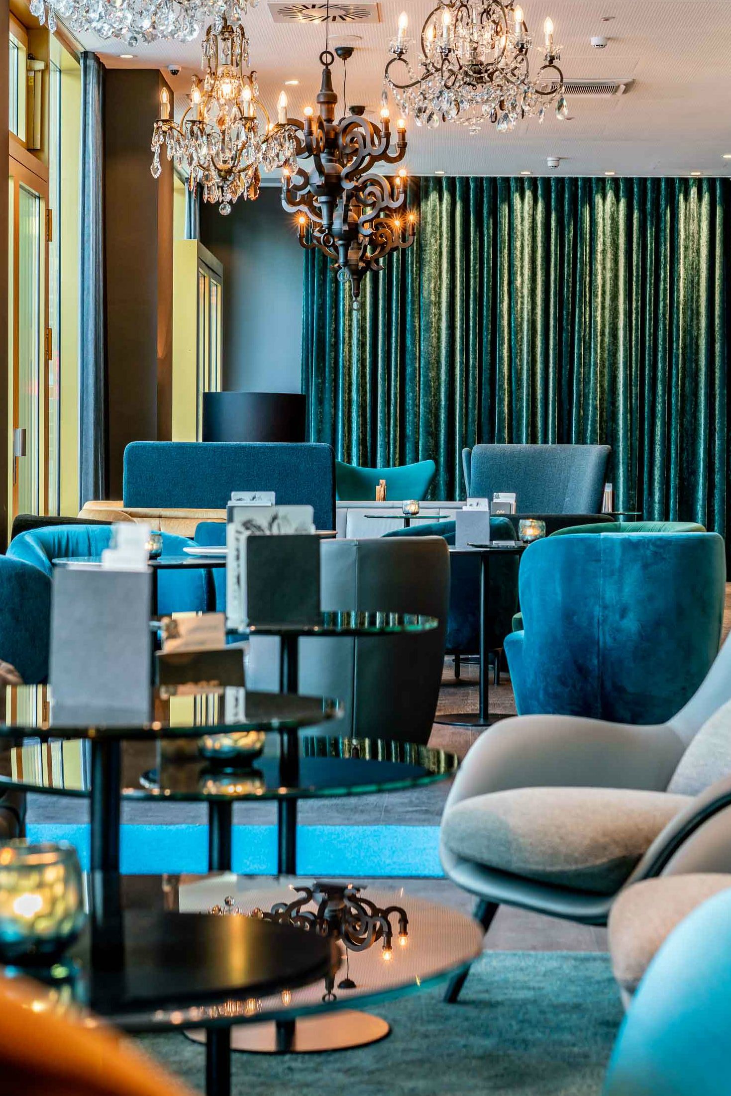 Hotel Berlin Ku’damm Motel One lichtdurchflutete Lounge mit mehreren Sesseln in unterschiedlichen Blautönen und Kronleuchter an der Decke