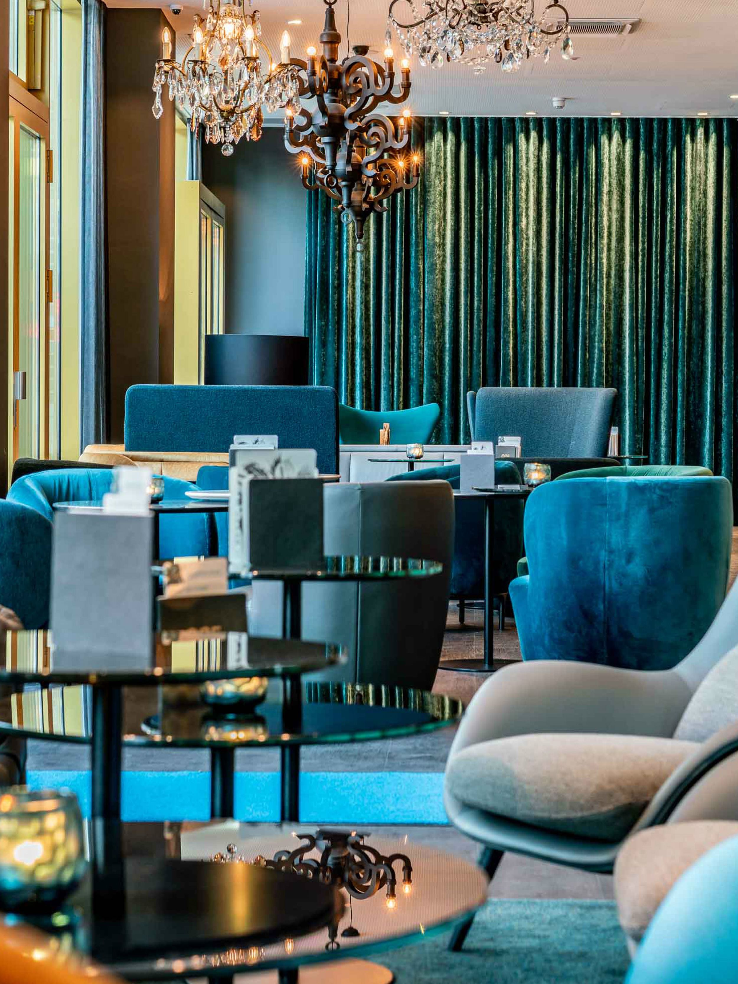 Hotel Berlin Ku’damm Motel One lichtdurchflutete Lounge mit mehreren Sesseln in unterschiedlichen Blautönen und Kronleuchter an der Decke