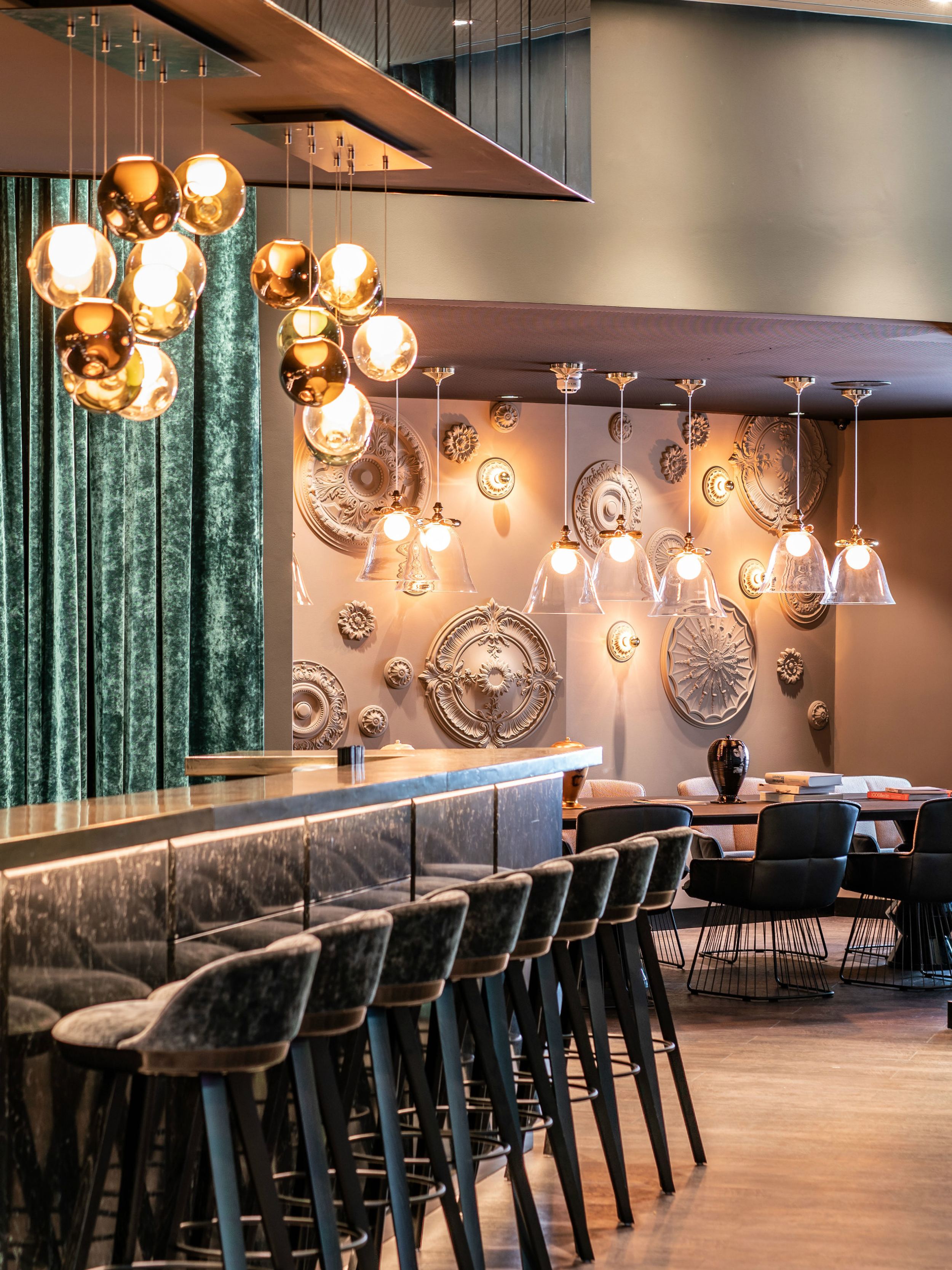 Designhotel Berlin Ku’damm Motel One helle Bar mit langer Theke und mehreren Barhockern sowie weitere Sitzgelegenheiten im Hintergrund