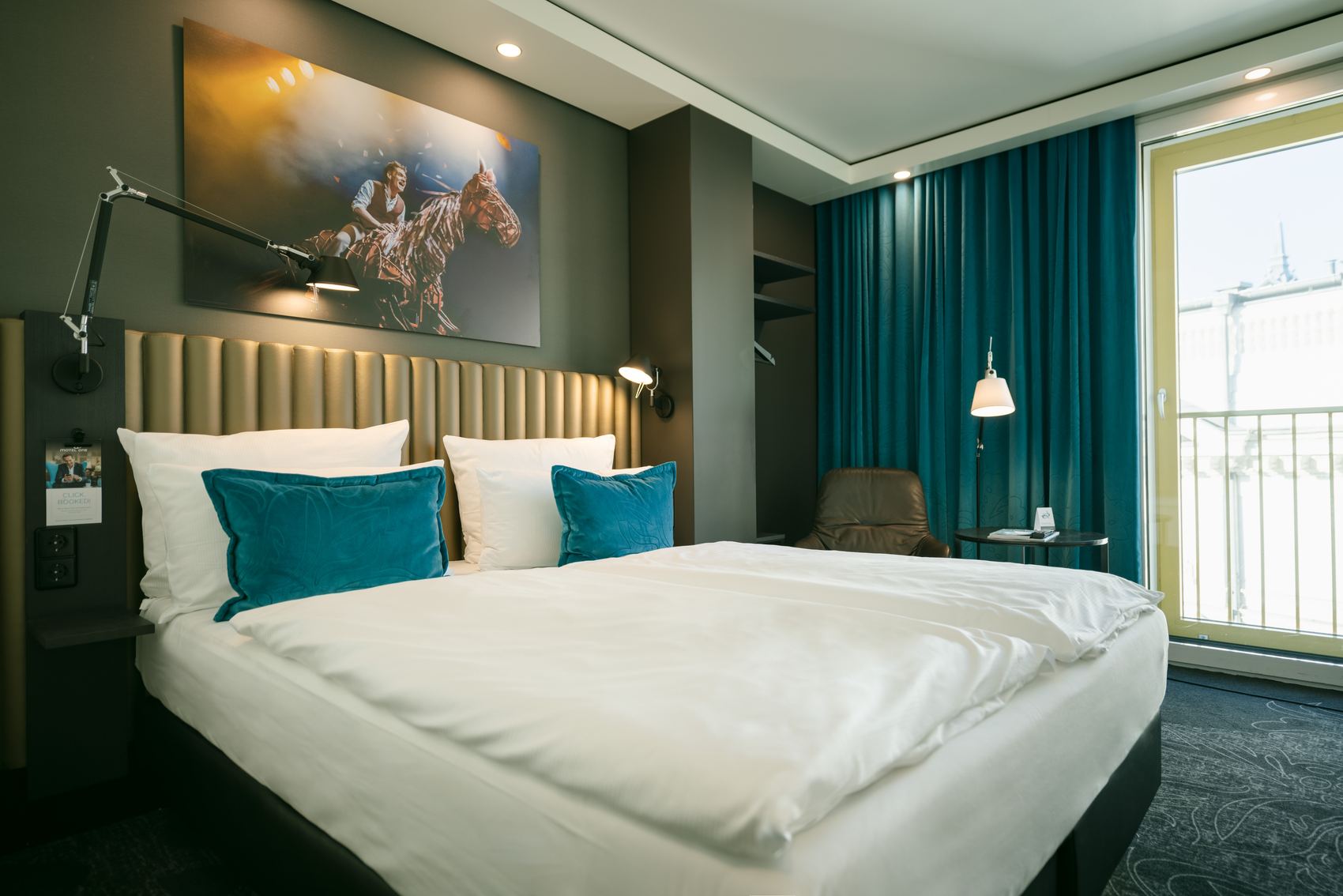 Designhotel Berlin Ku’damm Motel One helles Zimmer mit Doppelbett sowie Sessel und Beistelltisch vor bodentiefem Fenster