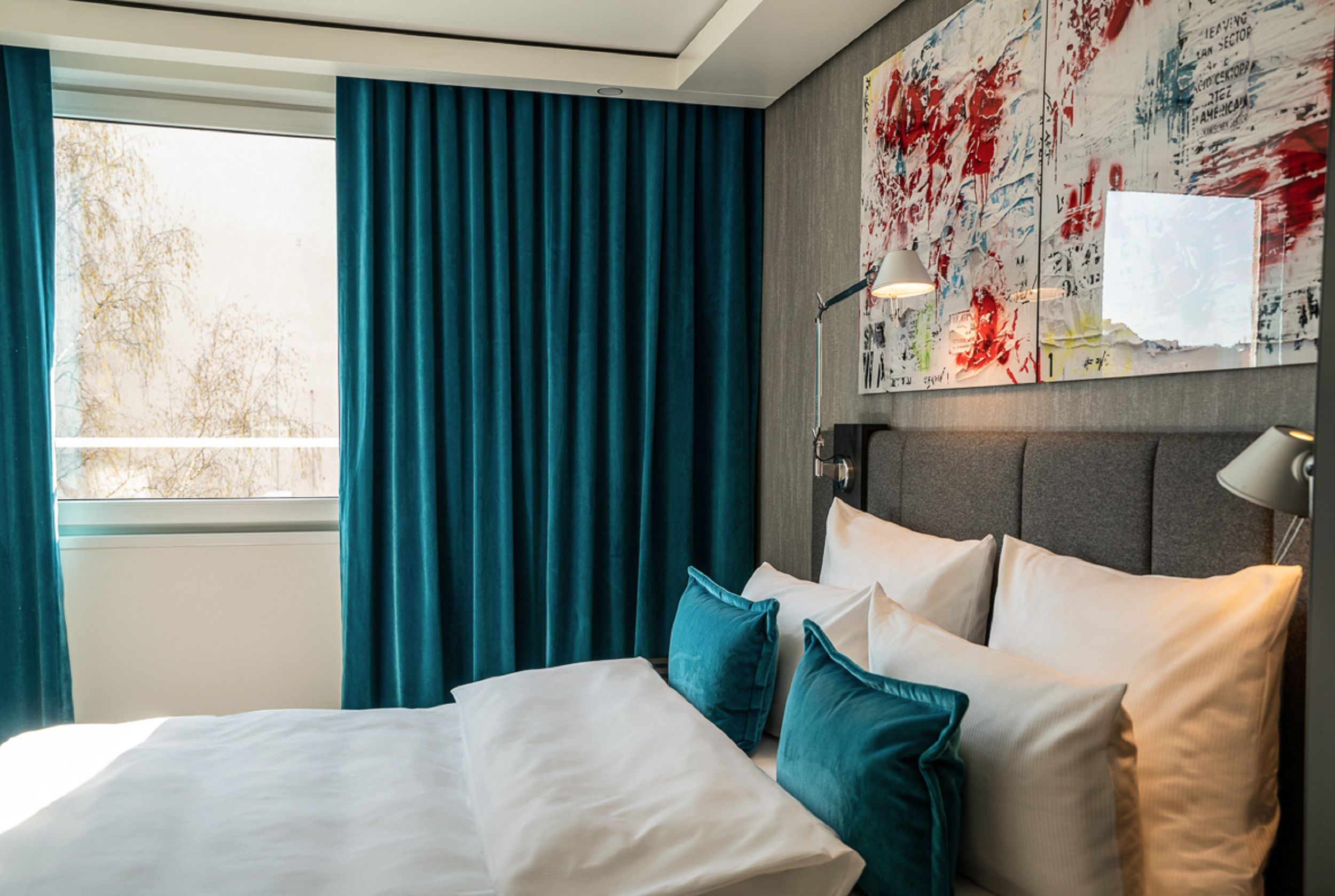hotel Berlin Mitte Motel One side view across a comfortable double bed with two decorative pillows to a large window with turquoise curtains