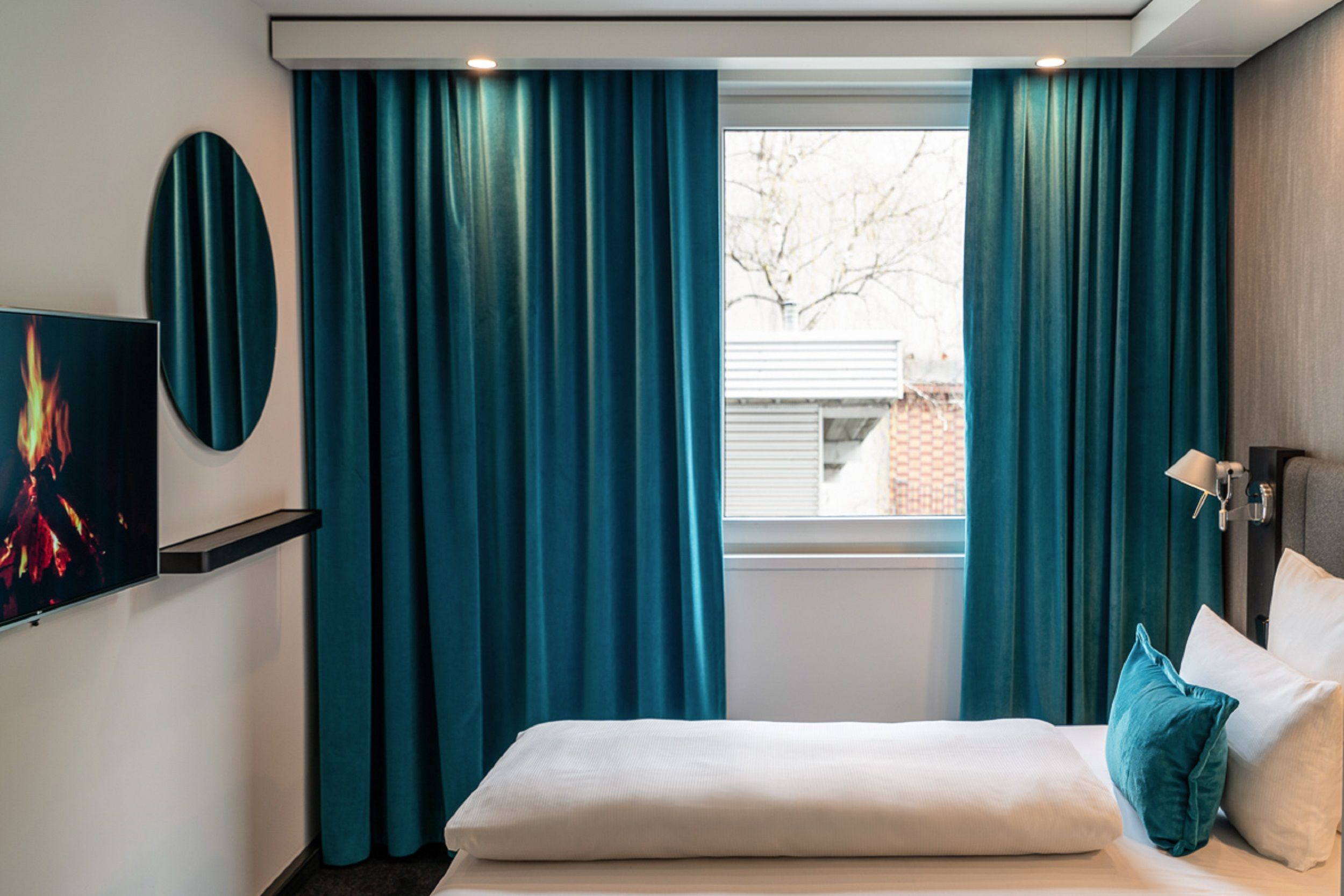 hotel Berlin Mitte Motel One bright room with a bed, a TV on the wall, a round mirror, and a large window