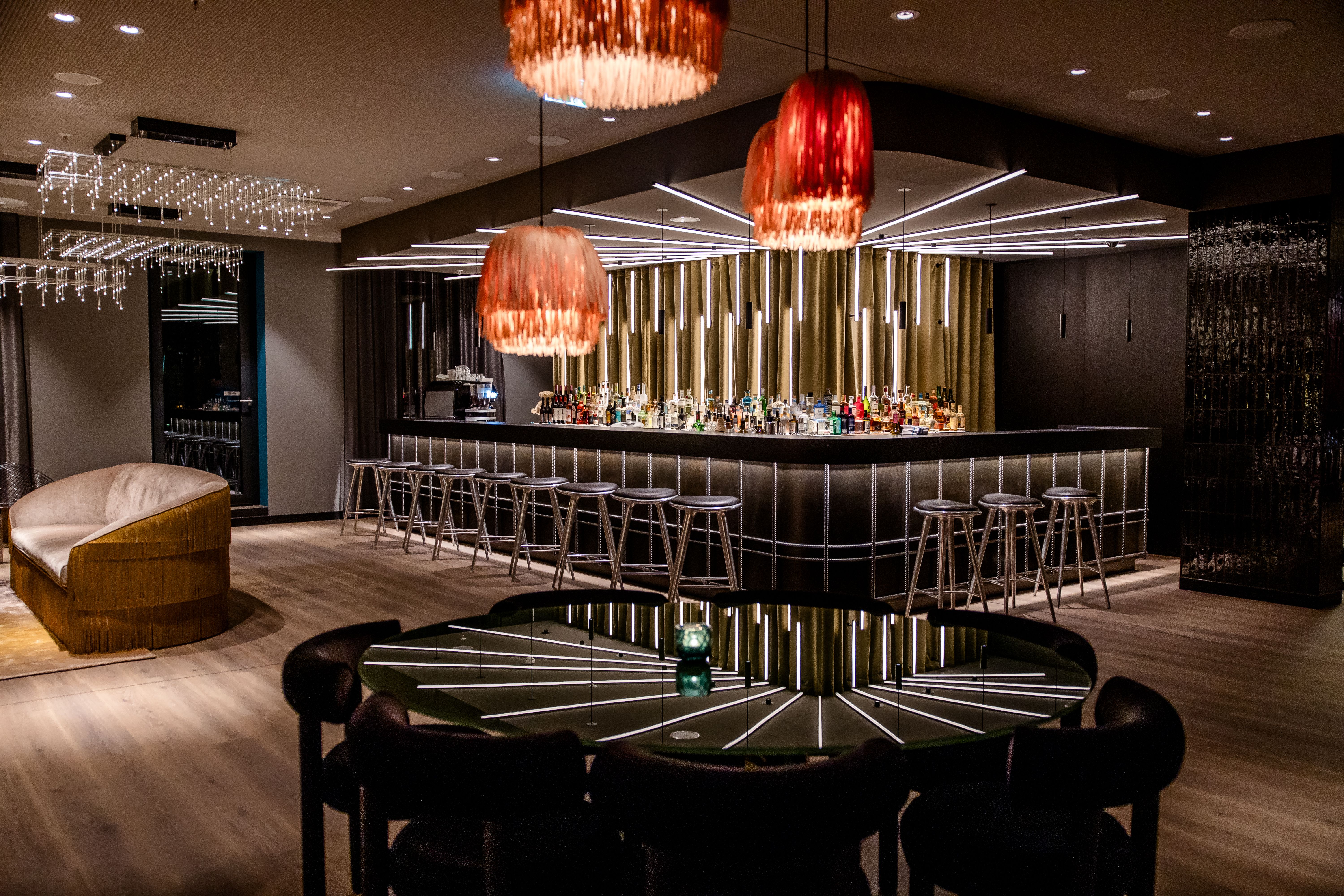 Hotel Berlin-Potsdamer Platz Motel One Elegante Hotelbar mit stilvollen Hockern, warmem Licht von roten Pendelleuchten und gemütlichen Sitzbereichen, die eine einladende Atmosphäre für entspannte Abende schaffen.