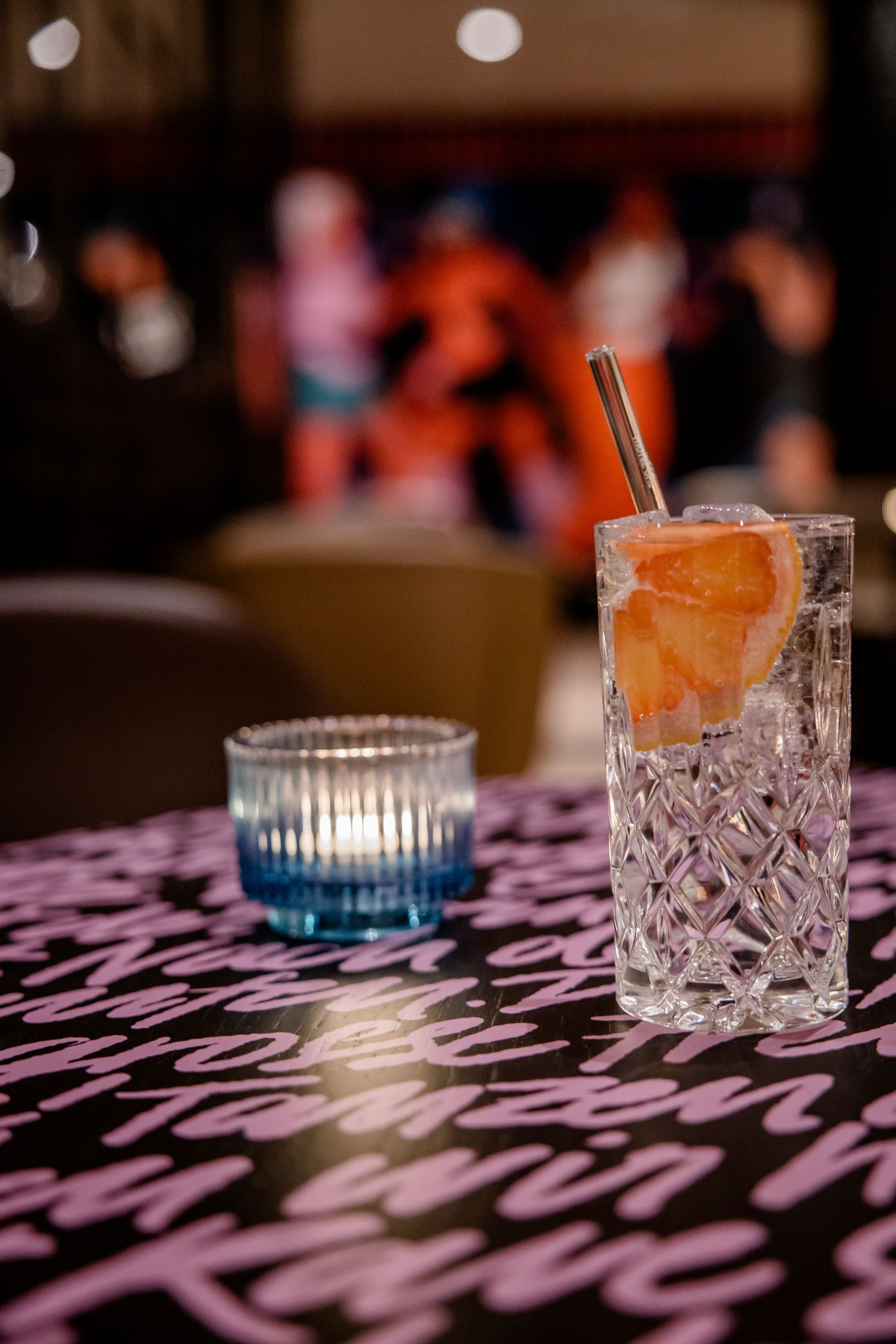 Hotel Berlin-Potsdamer Platz Motel One erfrischendes Getränk mit Eis und Grapefruitscheibe steht auf einem Tisch neben einer kleinen, brennenden Kerze. 