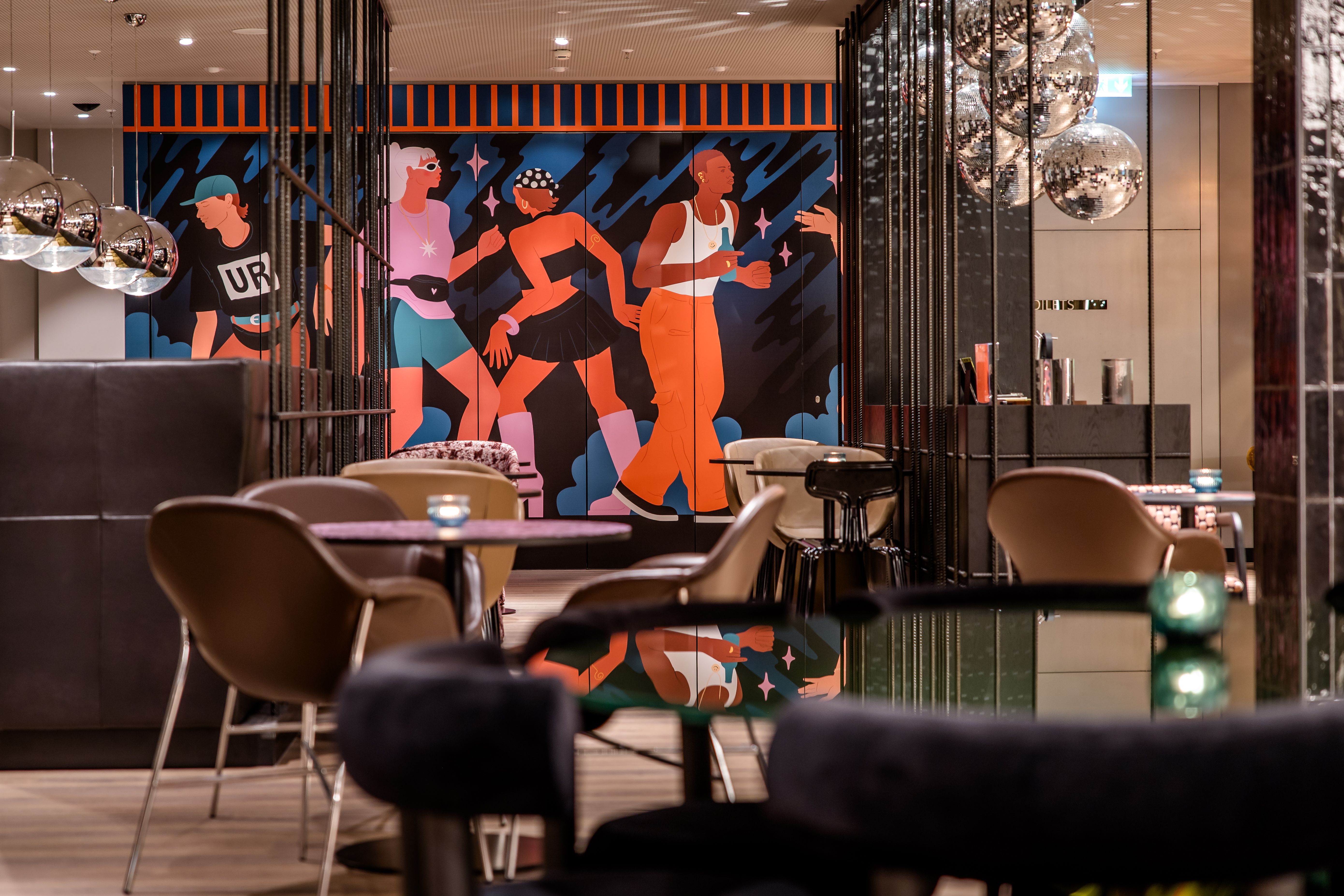 Hotel Berlin-Potsdamer Platz Motel One Moderne Hotelbar mit stilvoller Beleuchtung, gemütlichen Sitzgelegenheiten und farbenfrohem Wandbild mit dynamischen Figuren, die Bewegung und Lebendigkeit ausdrücken.