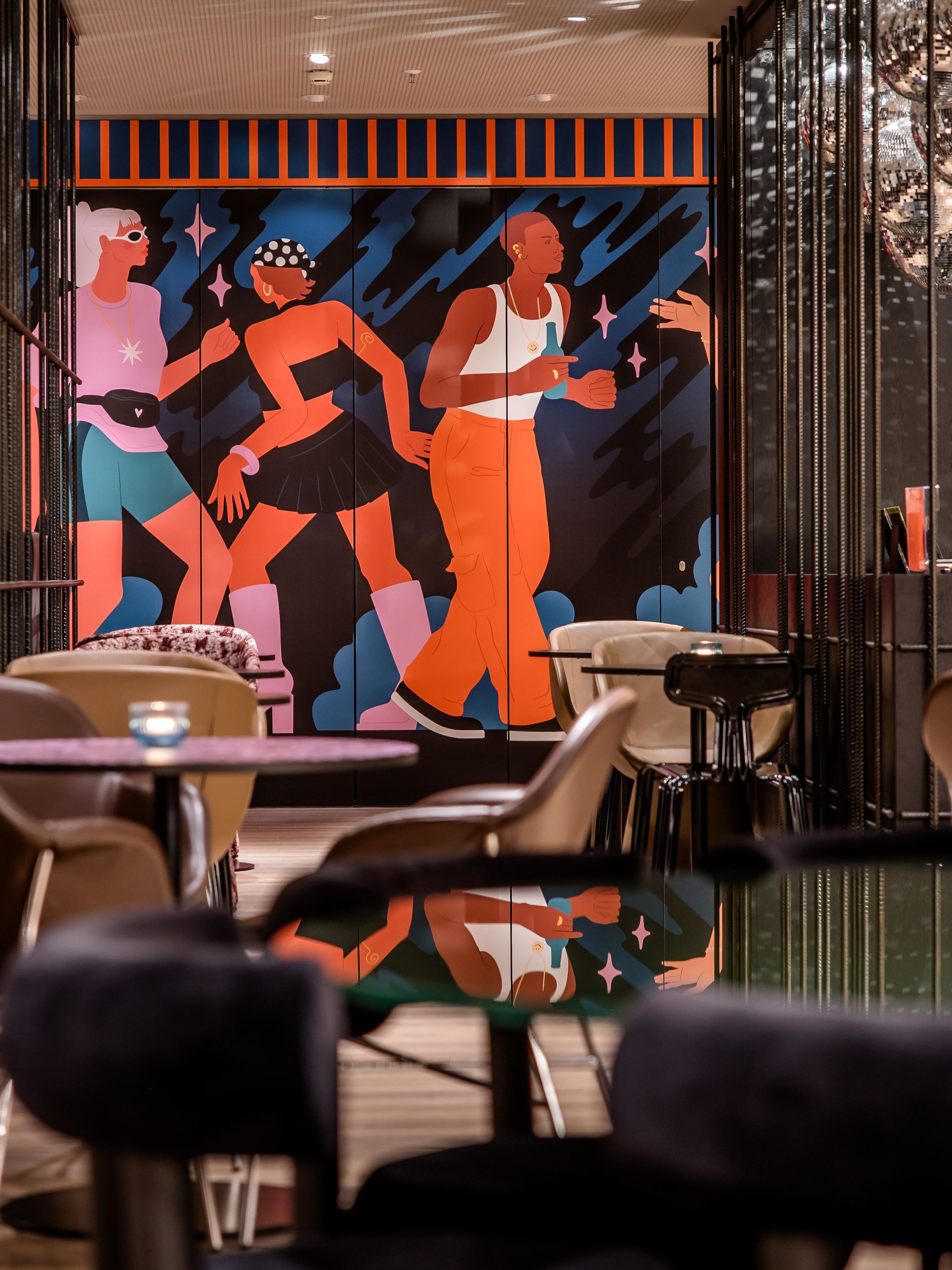 Hotel Berlin-Potsdamer Platz Motel One Moderne Hotelbar mit stilvoller Beleuchtung, gemütlichen Sitzgelegenheiten und farbenfrohem Wandbild mit dynamischen Figuren, die Bewegung und Lebendigkeit ausdrücken.