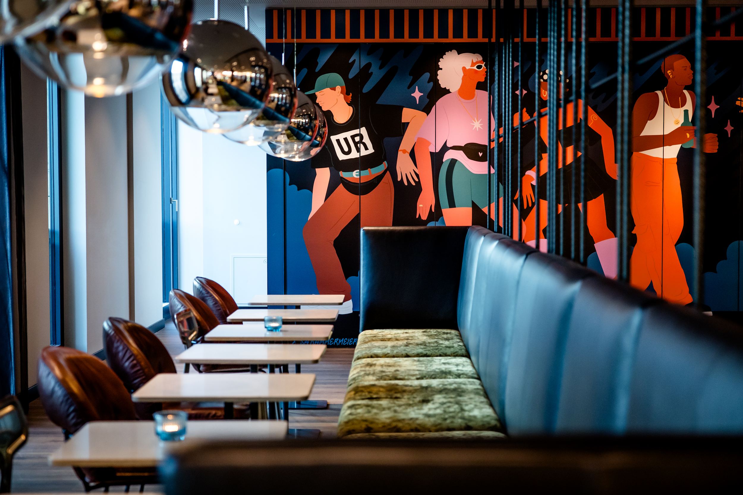 Hotel Berlin-Potsdamer Platz Motel One Moderner Restaurantbereich mit gemütlichen Sitzbänken, eleganten Tischen und stilvoller Wanddekoration mit farbenfrohen Figuren, die eine lebhafte Atmosphäre schaffen.