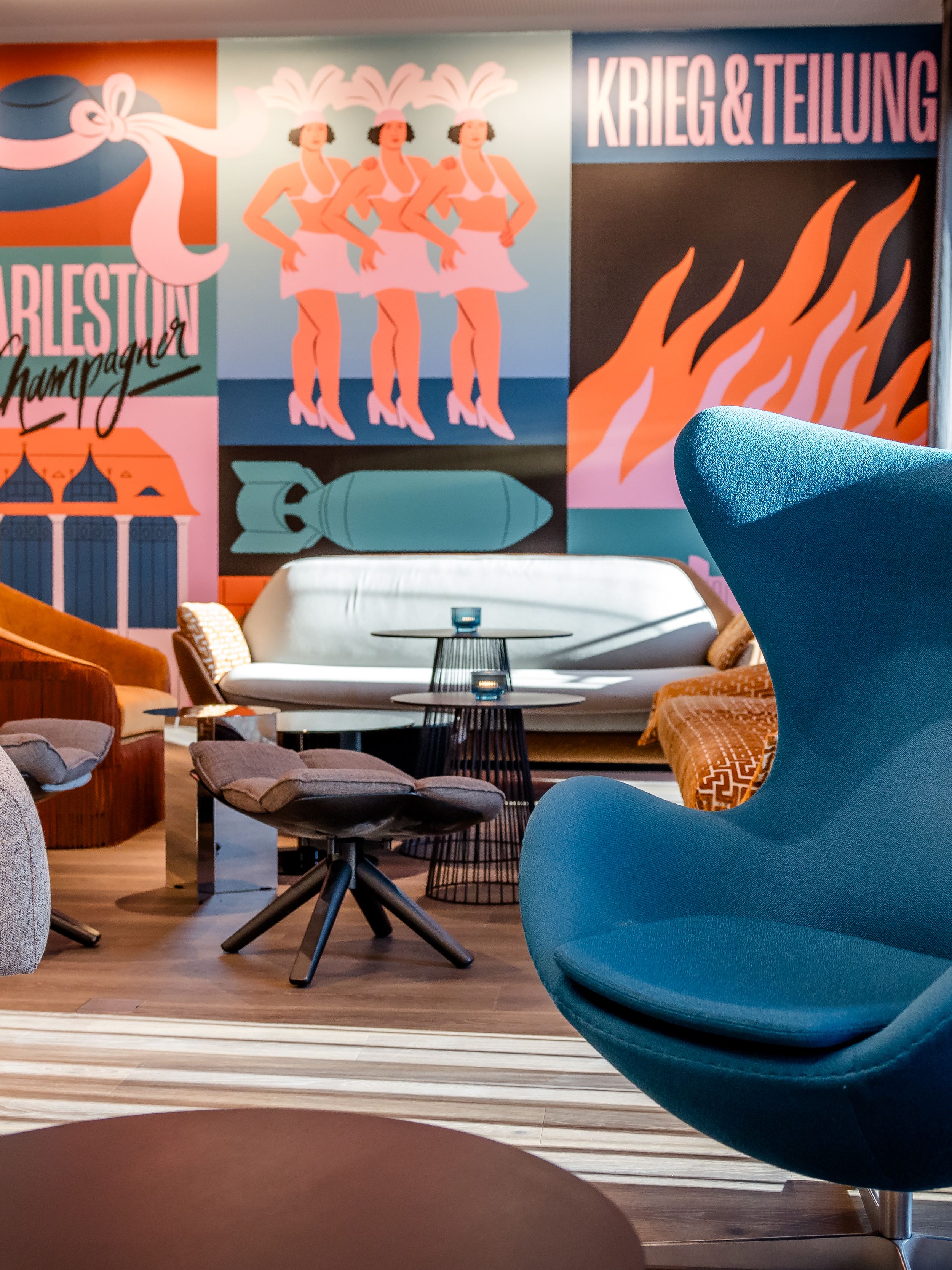 Hotel Berlin-Potsdamer Platz with One Lounge featuring modern armchairs and sofas in front of colourful retro-style murals depicting lively motifs and lettering. Bright, inviting atmosphere with stylish design and comfortable seating for relaxing moments.
