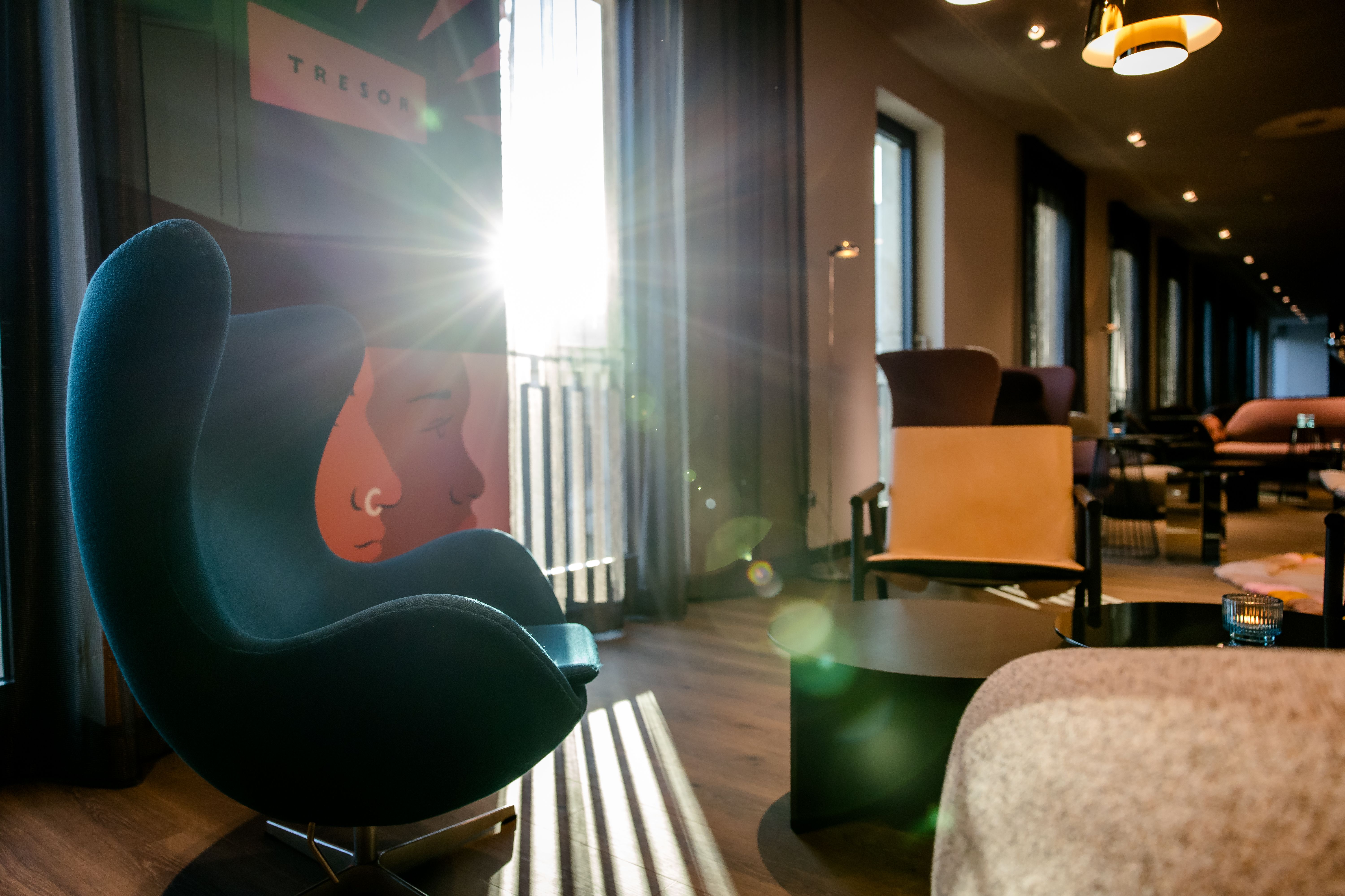 Hotel Berlin-Potsdamer Platz Motel One Lounge-Bereich mit modernen Sesseln und Sofas, warmes Sonnenlicht strahlt durch große Fenster, einladende Atmosphäre zum Entspannen und Verweilen.