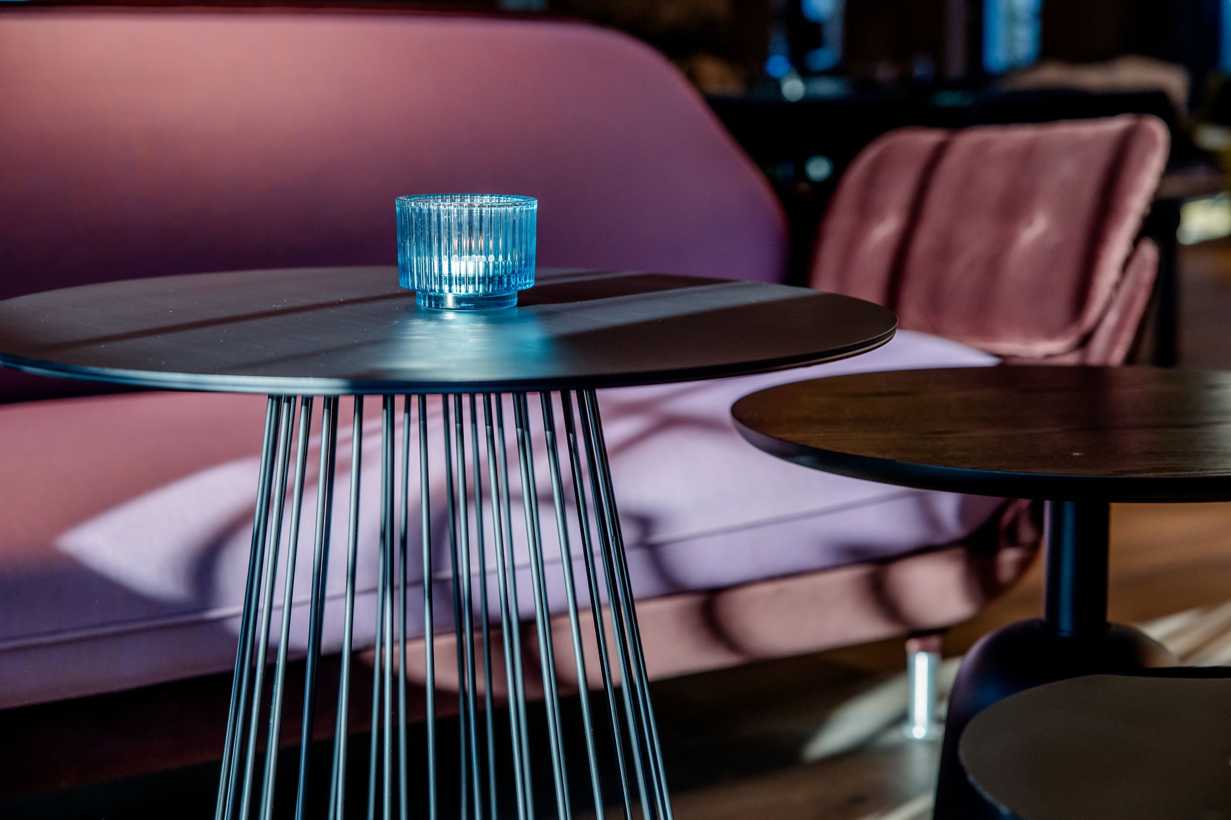 Hotel Berlin-Potsdamer Platz Motel One Moderner Sitzbereich mit stilvollen, runden Metalltischen und einem rosa gepolsterten Sofa, auf einem Tisch steht ein blauer, dekorativer Kerzenhalter für eine gemütliche Atmosphäre.