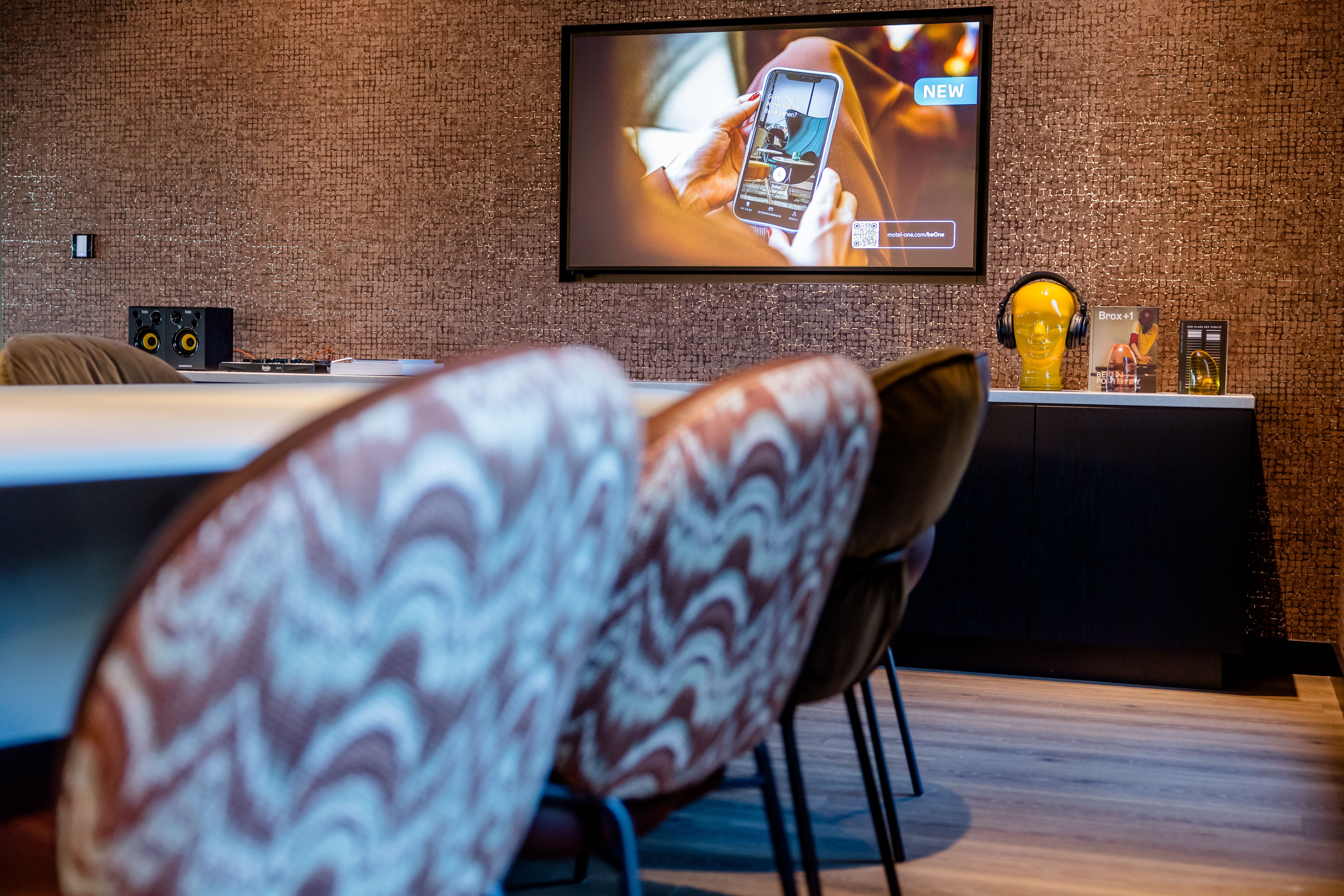Hotel Berlin-Potsdamer Platz Motel One Moderner Konferenzraum mit komfortablen Stühlen, einer großen Wandbildschirmanzeige und gedämpfter, einladender Beleuchtung.
