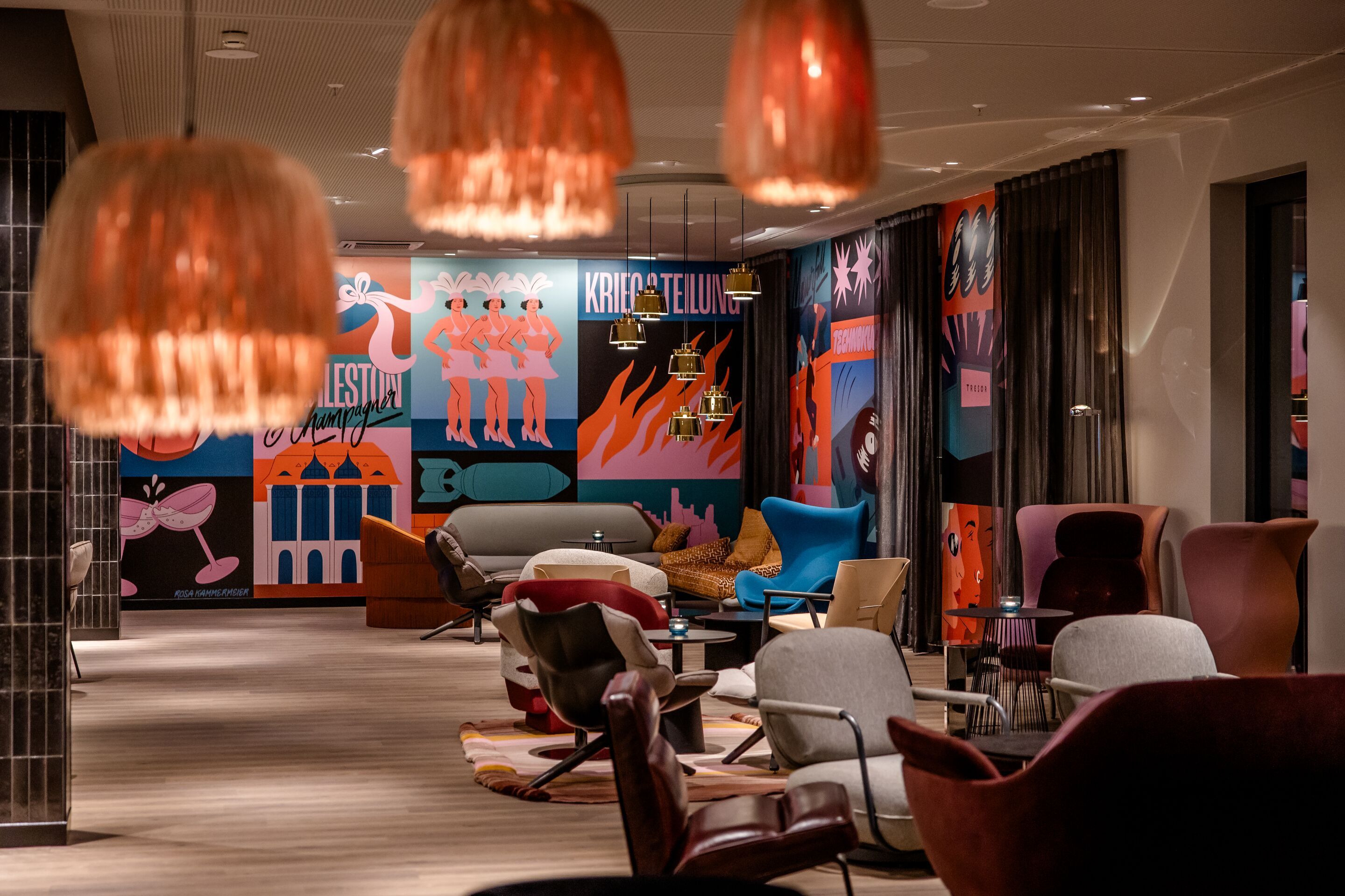 Hotel Berlin Potsdamer Platz Motel One modern lounge with colourful, artistic murals, stylish armchairs and sofas bathed in warm light, ideal for relaxing and socialising.