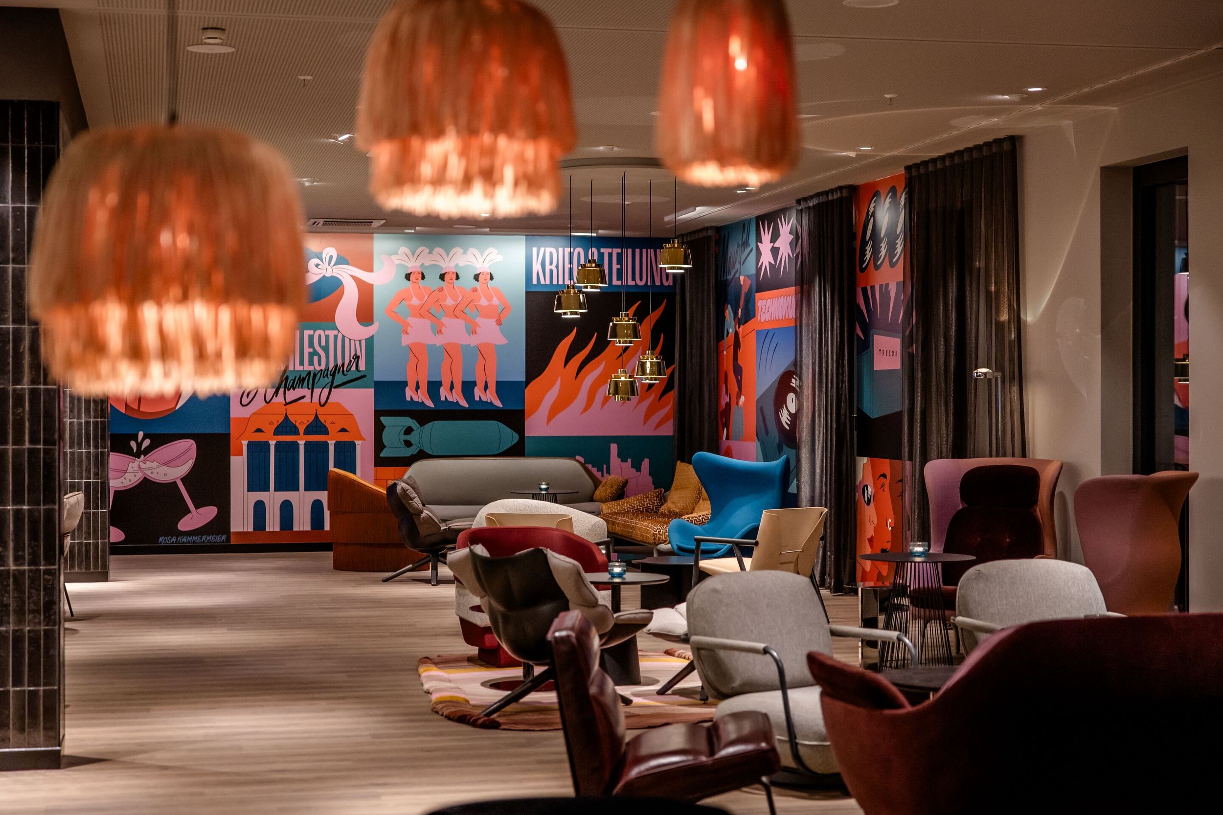 Hotel Berlin Potsdamer Platz Motel One modern lounge with colourful, artistic murals, stylish armchairs and sofas bathed in warm light, ideal for relaxing and socialising.