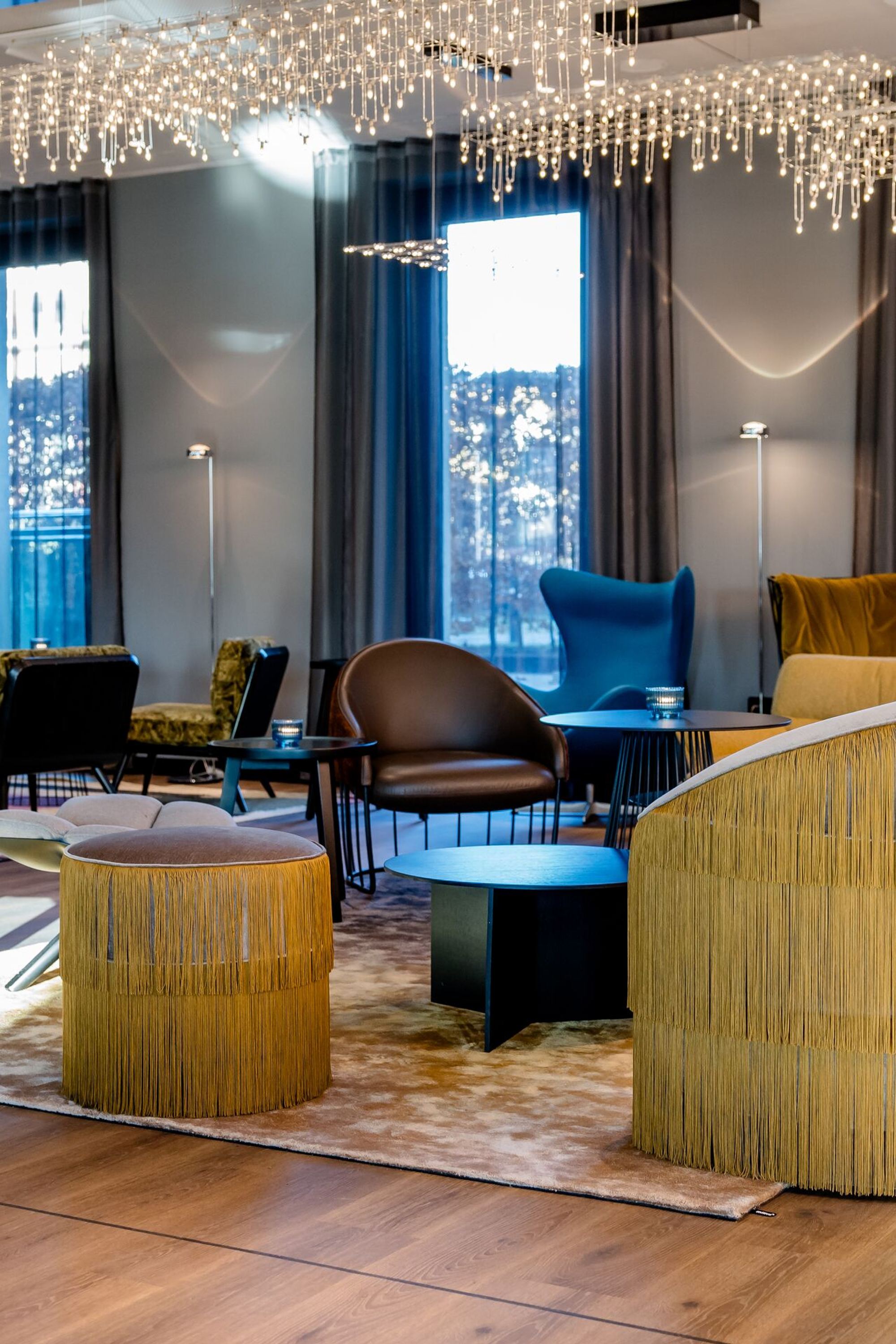 Hotel Berlin Potsdamer Platz Motel One moderne, helle Lounge mit stilvollen Sesseln und Sofas, großen Fenstern und elegantem Kronleuchter, der eine gemütliche und einladende Atmosphäre schafft.