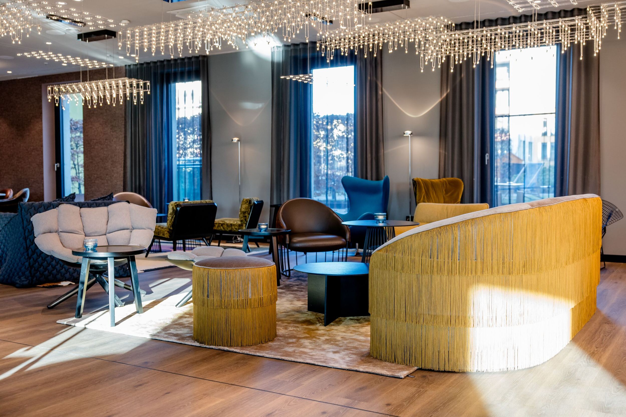 Hotel Berlin Potsdamer Platz Motel One moderne, helle Lounge mit stilvollen Sesseln und Sofas, großen Fenstern und elegantem Kronleuchter, der eine gemütliche und einladende Atmosphäre schafft.