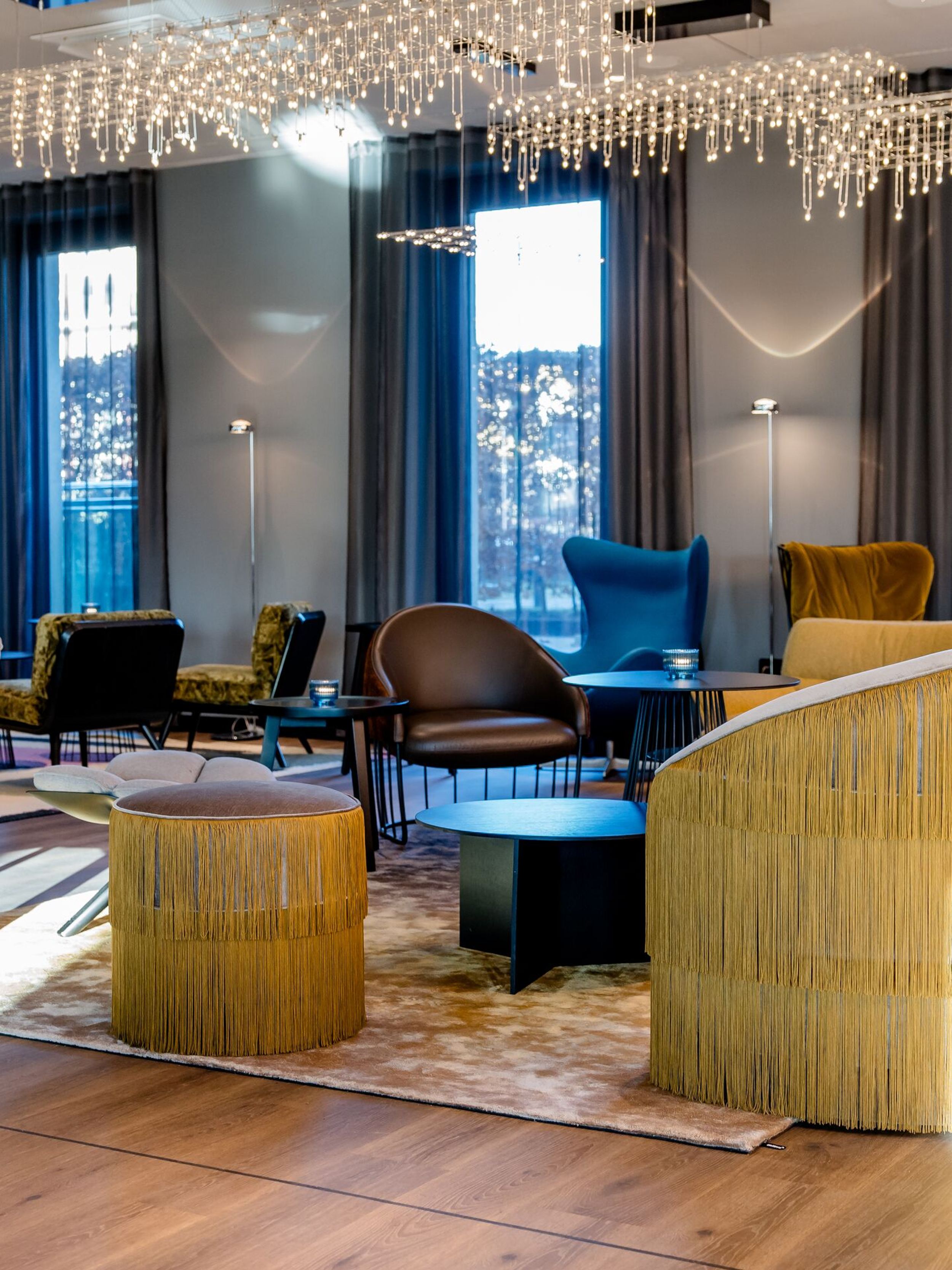 Hotel Berlin Potsdamer Platz Motel One moderne, helle Lounge mit stilvollen Sesseln und Sofas, großen Fenstern und elegantem Kronleuchter, der eine gemütliche und einladende Atmosphäre schafft.