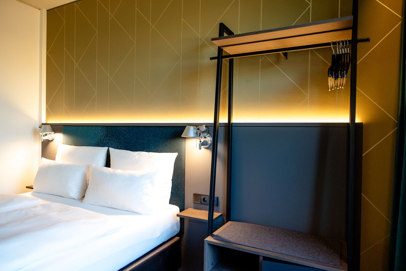 Hotel Berlin-Potsdamer Platz Motel One - Gemütliches Hotelzimmer mit großem Bett, weichen Kissen, sanfter Beleuchtung und offenem Kleiderständer für bequeme Garderobenaufbewahrung.