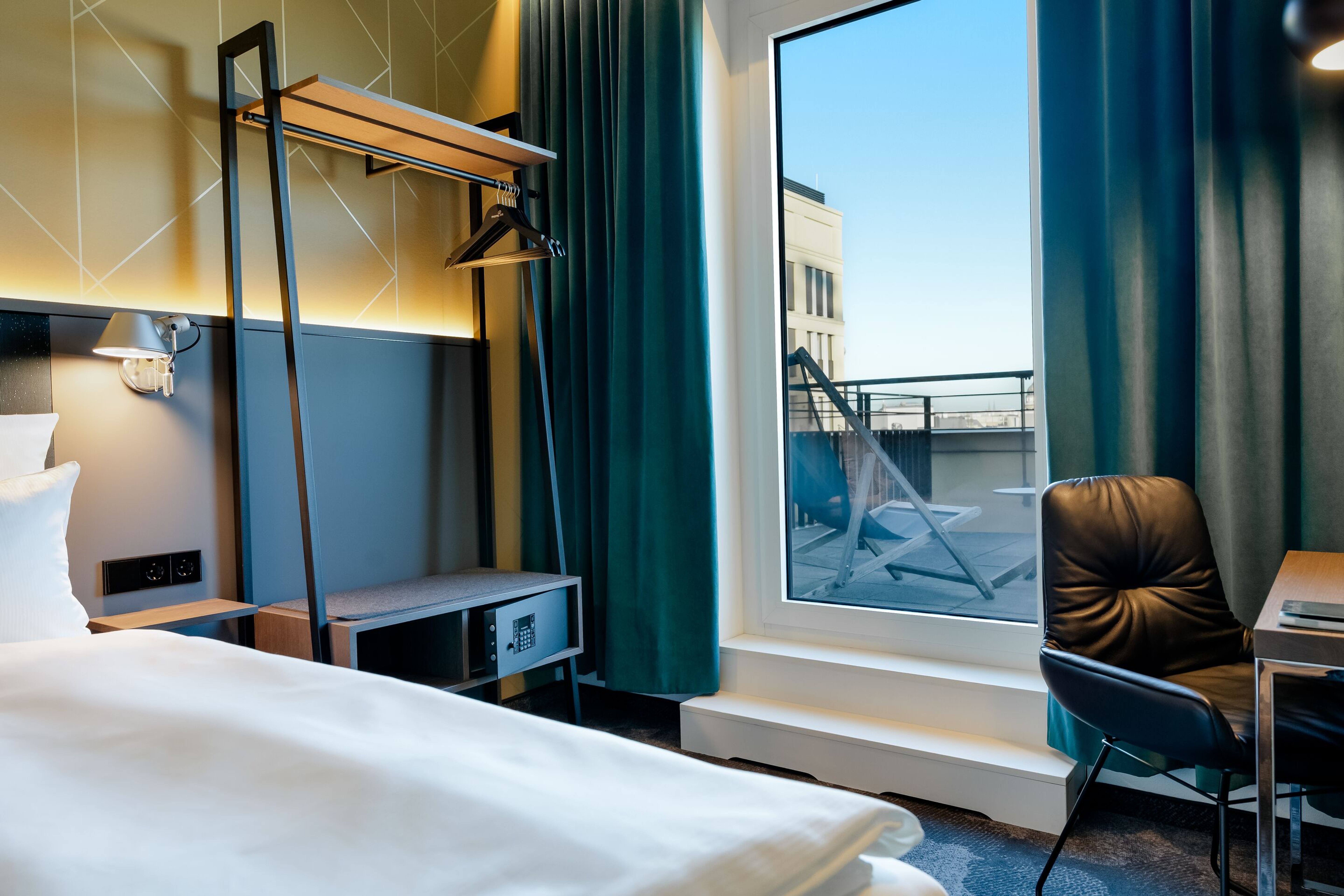 Hotel Berlin-Potsdamer Platz Motel One - Modern eingerichtetes Hotelzimmer mit großem Fenster und Zugang zu einer Terrasse, komfortables Bett, Schreibtisch mit Stuhl, offene Garderobe und beruhigende Farbgestaltung in Blau- und Grautönen. Hotel Berlin-Potsdamer Platz Motel One - Modern eingerichtetes Hotelzimmer mit großem Fenster und Zugang zu einer Terrasse, komfortables Bett, Schreibtisch mit Stuhl, offene Garderobe und beruhigende Farbgestaltung in Blau- und Grautönen.