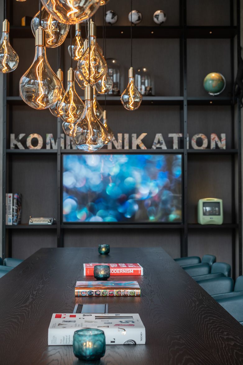 Hotel Berlin Spittelmarkt Motel One langer Tisch mit drei Büchern und Stühlen zum Sitzen sowie offenes Regal mit Schriftzug "Kommunikation"
