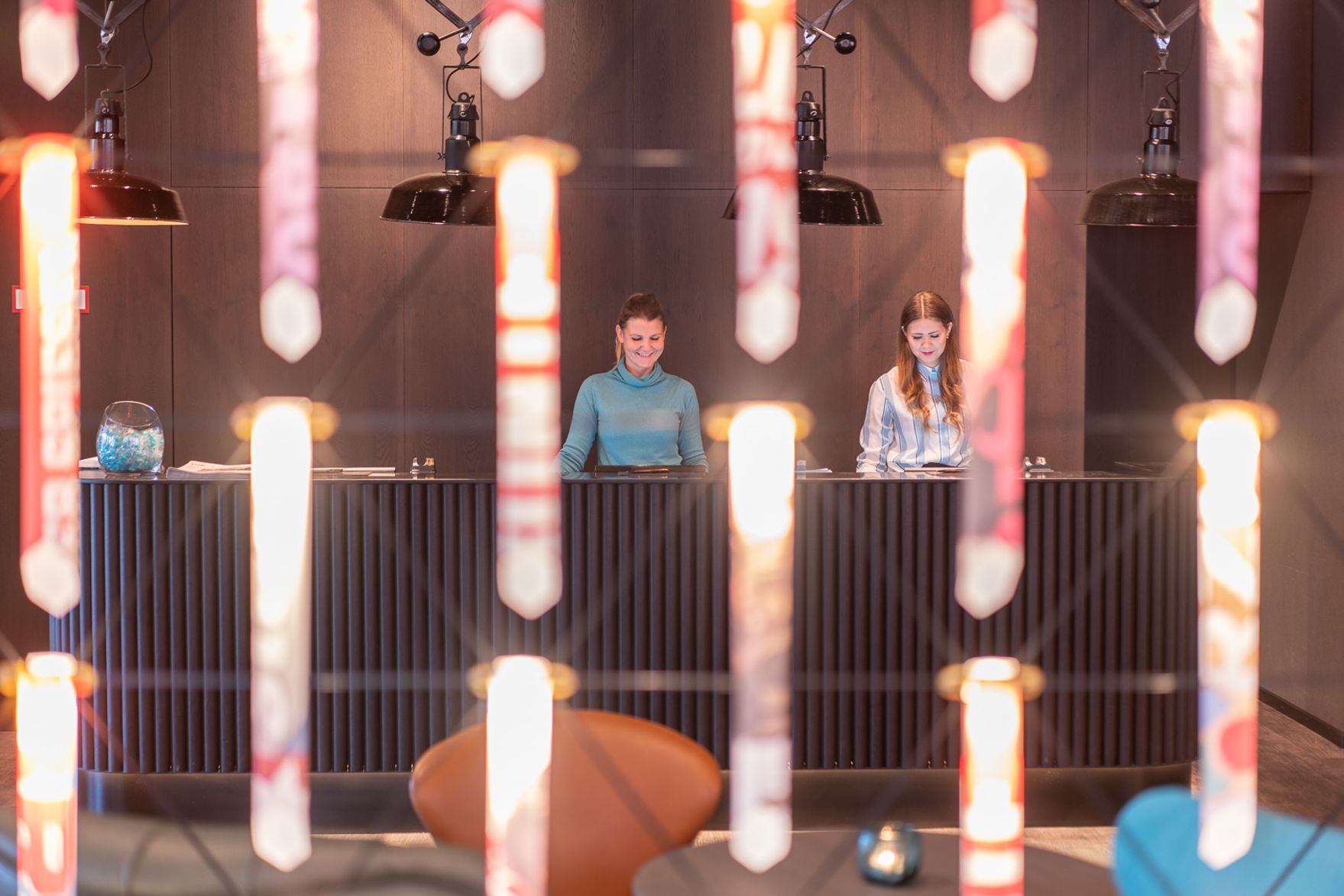 Designhotel Berlin Spittelmarkt Motel One Blick durch Lichter hin zur großen Rezeption mit zwei Mitarbeiterinnen