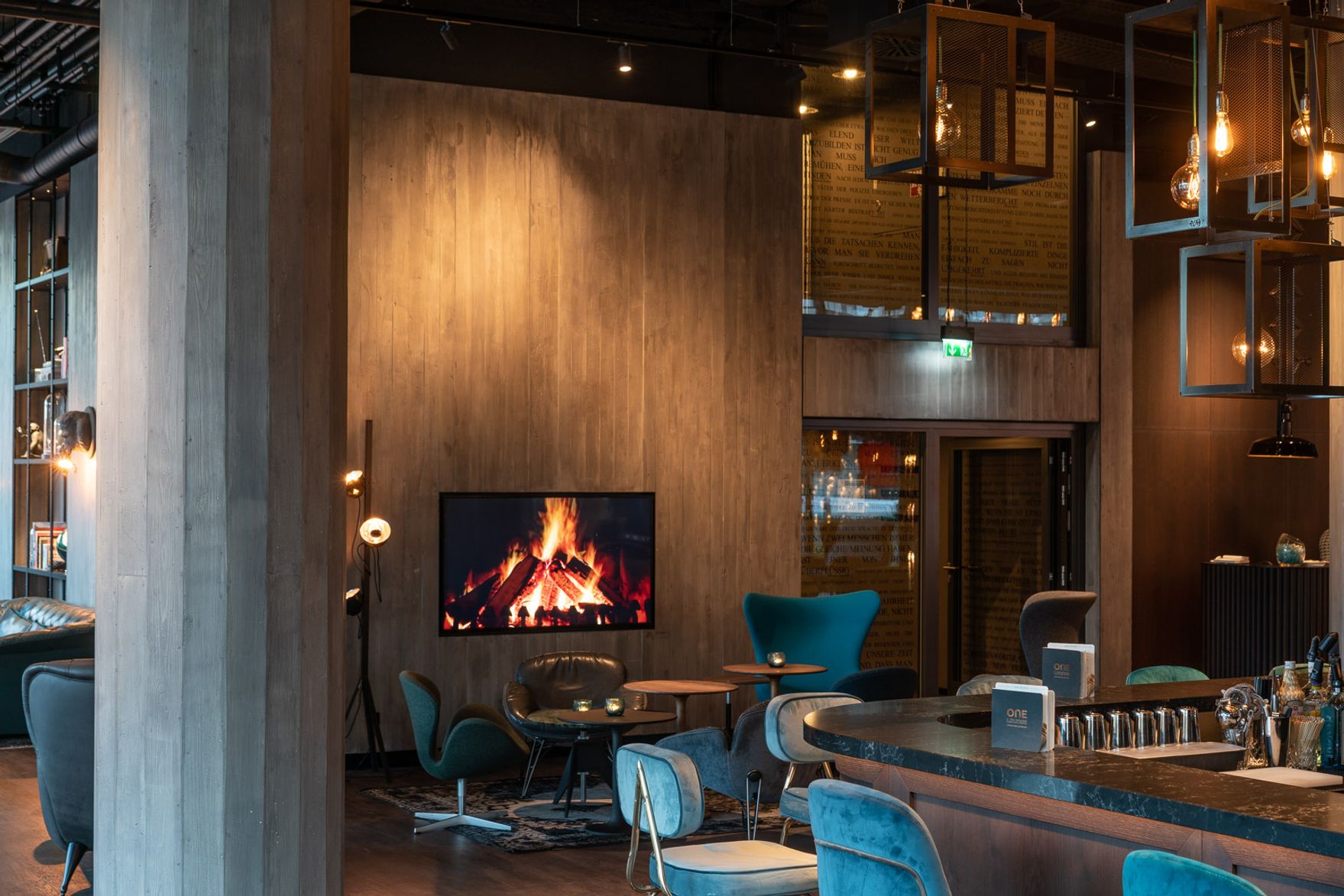 Designhotel Berlin Spittelmarkt Motel One große Lounge und Barbereich mit Sesseln und Fernseher mit Feuermotiv an der Wand