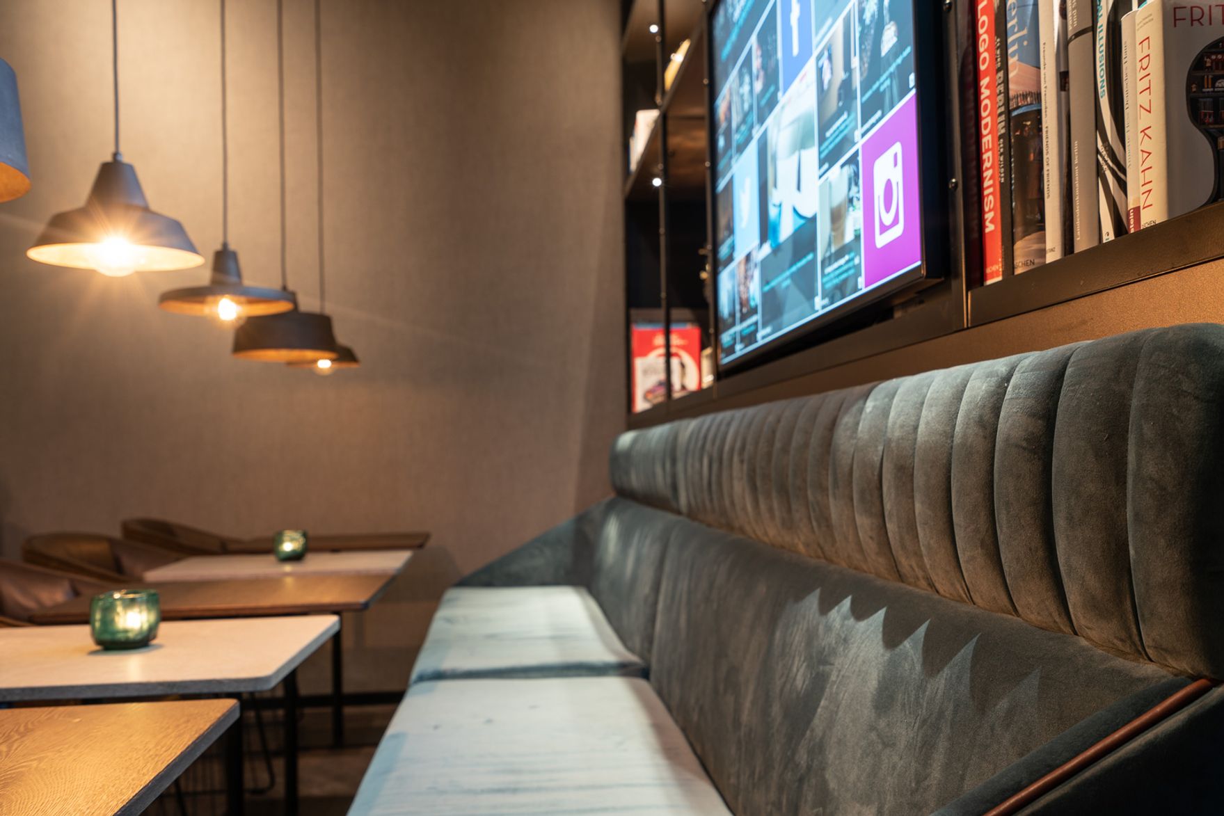 Designhotel Berlin Spittelmarkt Motel One Essbereich mit langem Sofa und mehreren Tischen daran