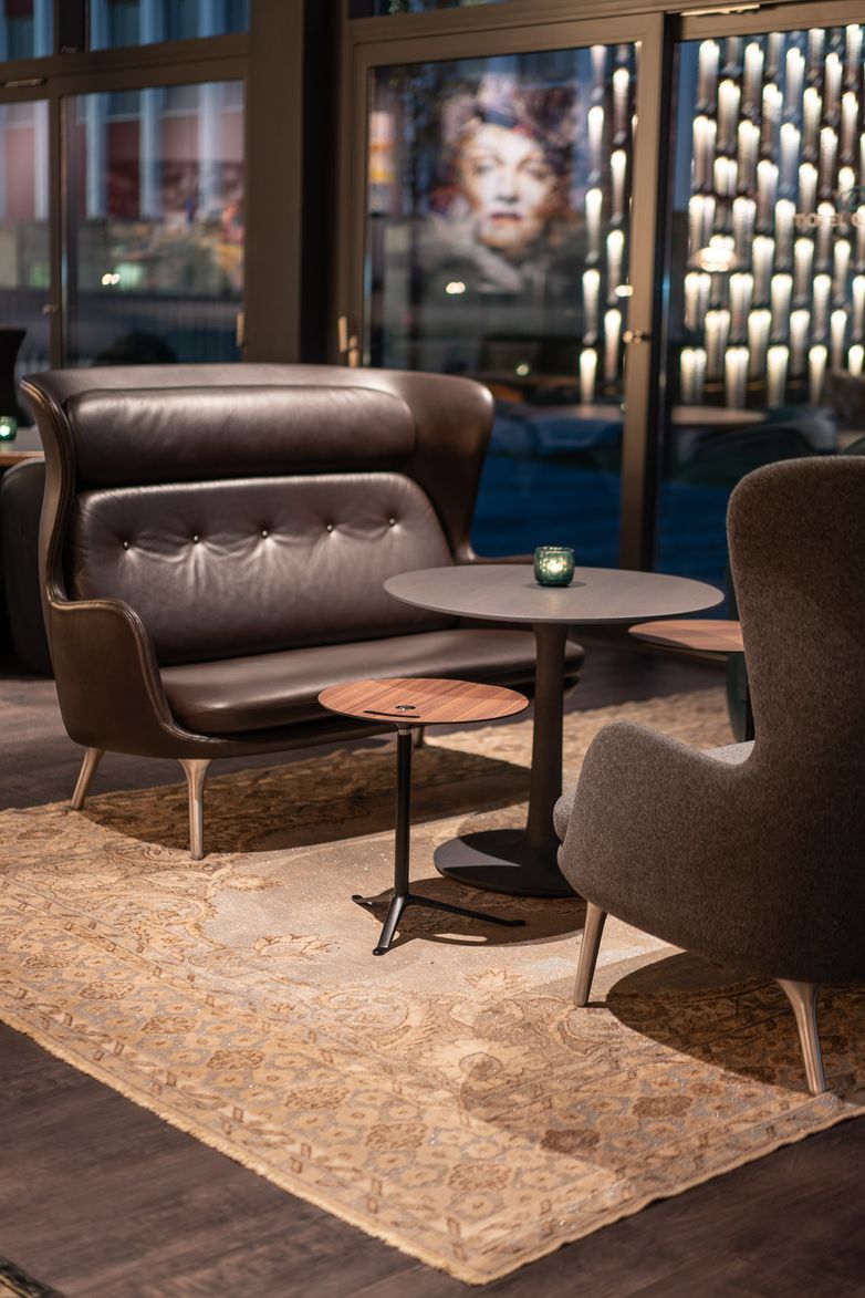 Designhotel Berlin Spittelmarkt Motel One Lounge bei Abend mit Blick auf zwei Sessel und drei Beistelltische in der Mitte sowie ein heller Teppich