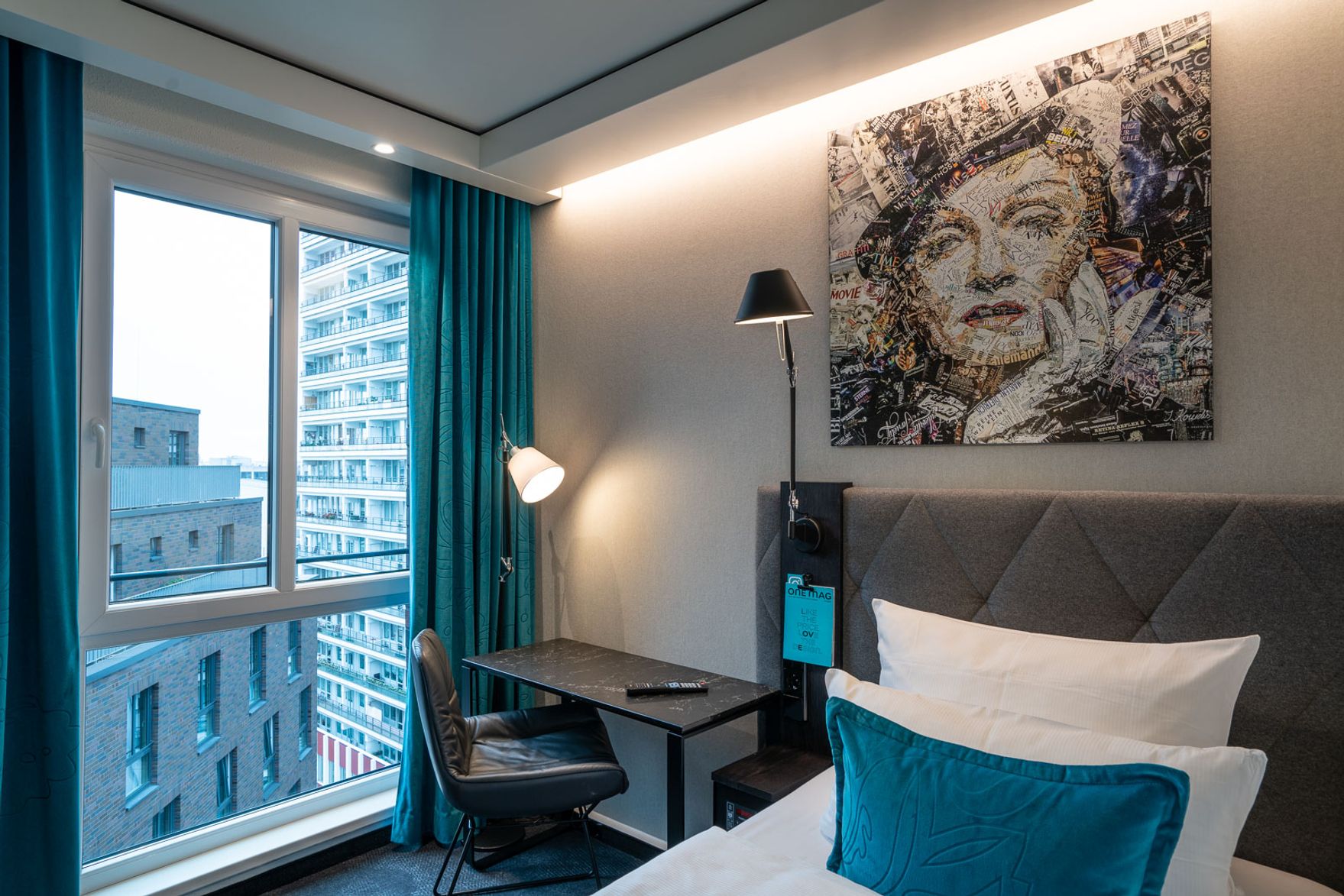 Hotel Berlin Spittelmarkt Motel One Zimmer mit Bett, Schreibtisch und Stuhl sowie Stehlampe vor einem bodentiefen Fenster