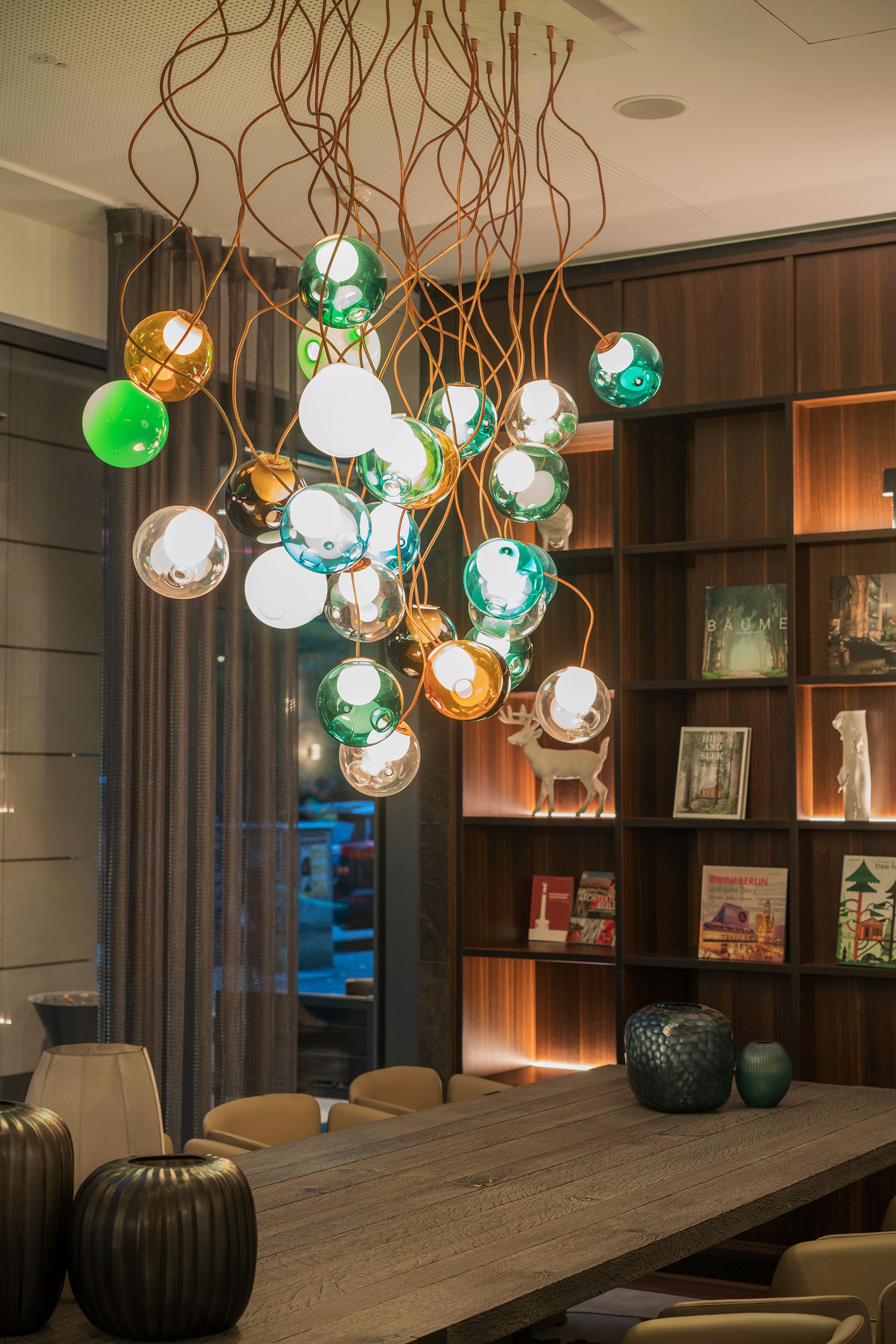Hotel Berlin Tiergarten Motel One Raum mit langem Tisch und mehreren Stühlen sowie eine Designerlampe mit runden bunten Gläsern als Lampenschirme