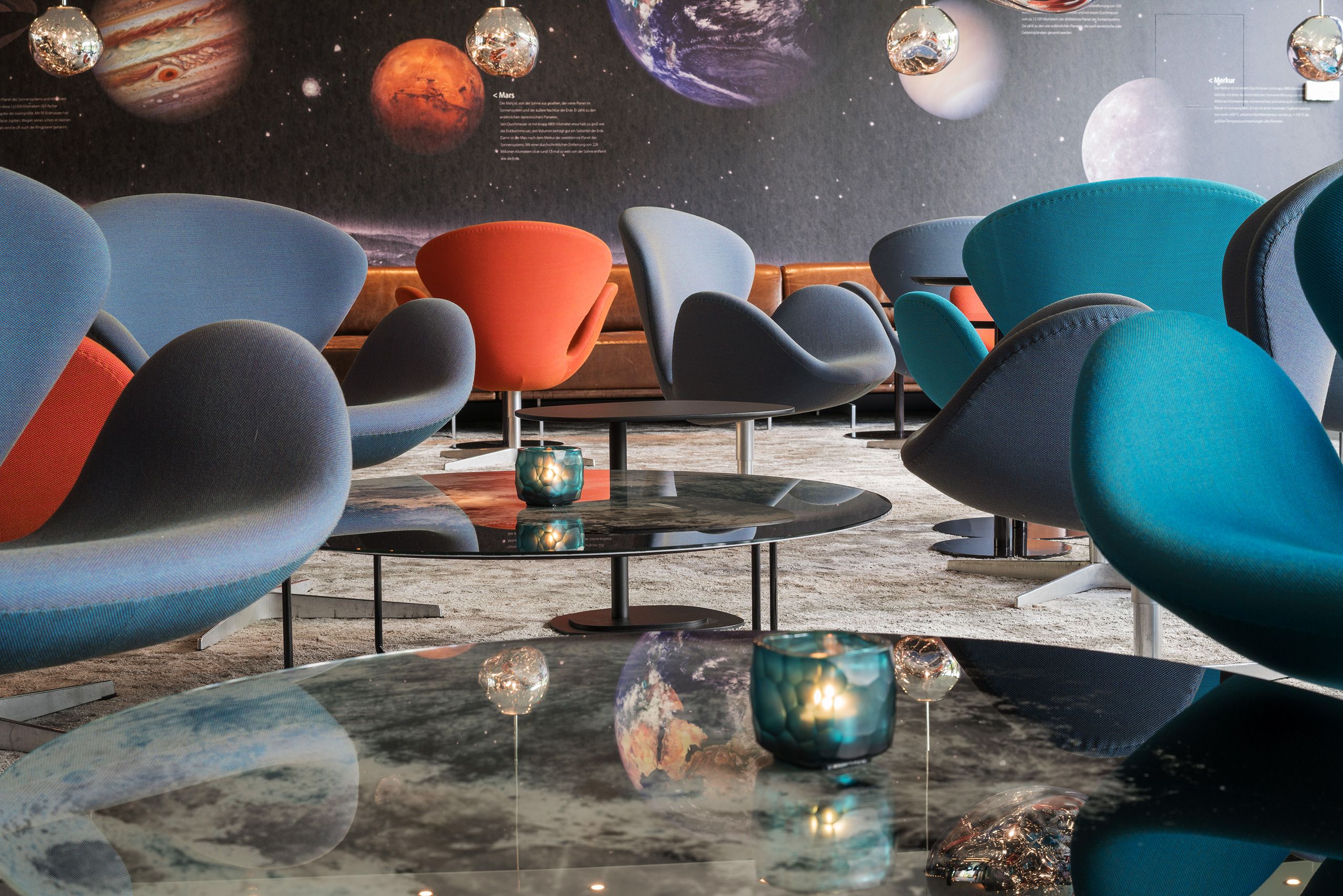 Hotel Berlin Tiergarten Motel One helle Lounge mit mehreren Sesseln und Beistelltischen sowie eine Wand mit den Planeten des Universums