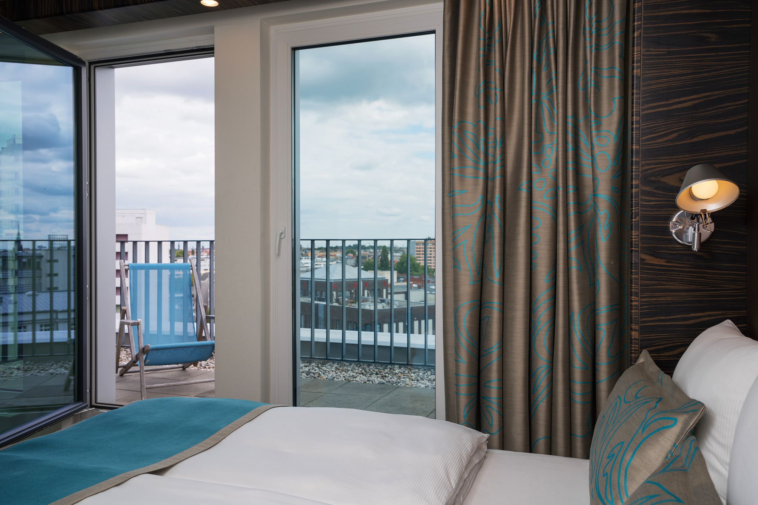 Designhotel Berlin Tiergarten Motel One helles Balkonzimmer mit seitlichem Blick über das Bett auf den Balkon mit Liegestuhl