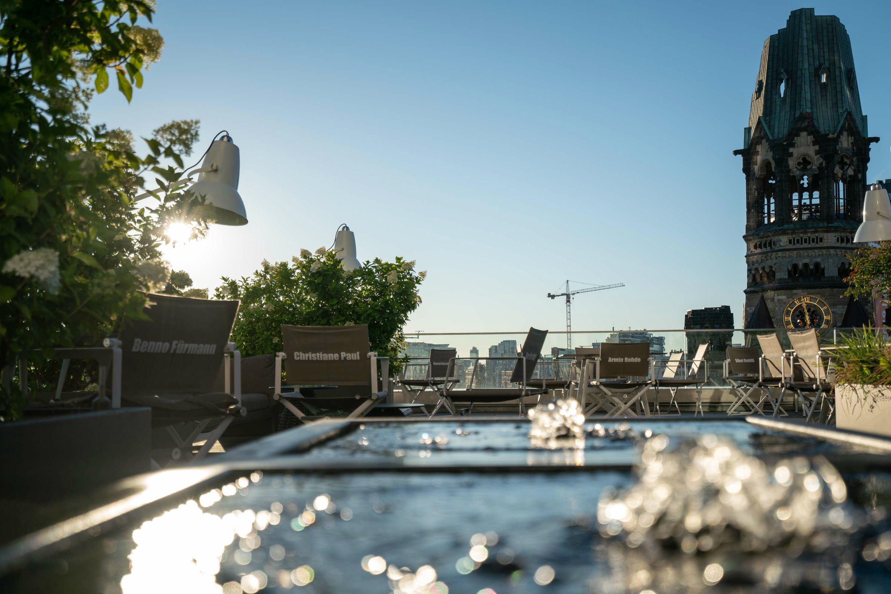 Designhotel Berlin Upper West Motel One Dachterrasse mit Blick auf mehrere Stühle und eine Kirche im Hintergrund