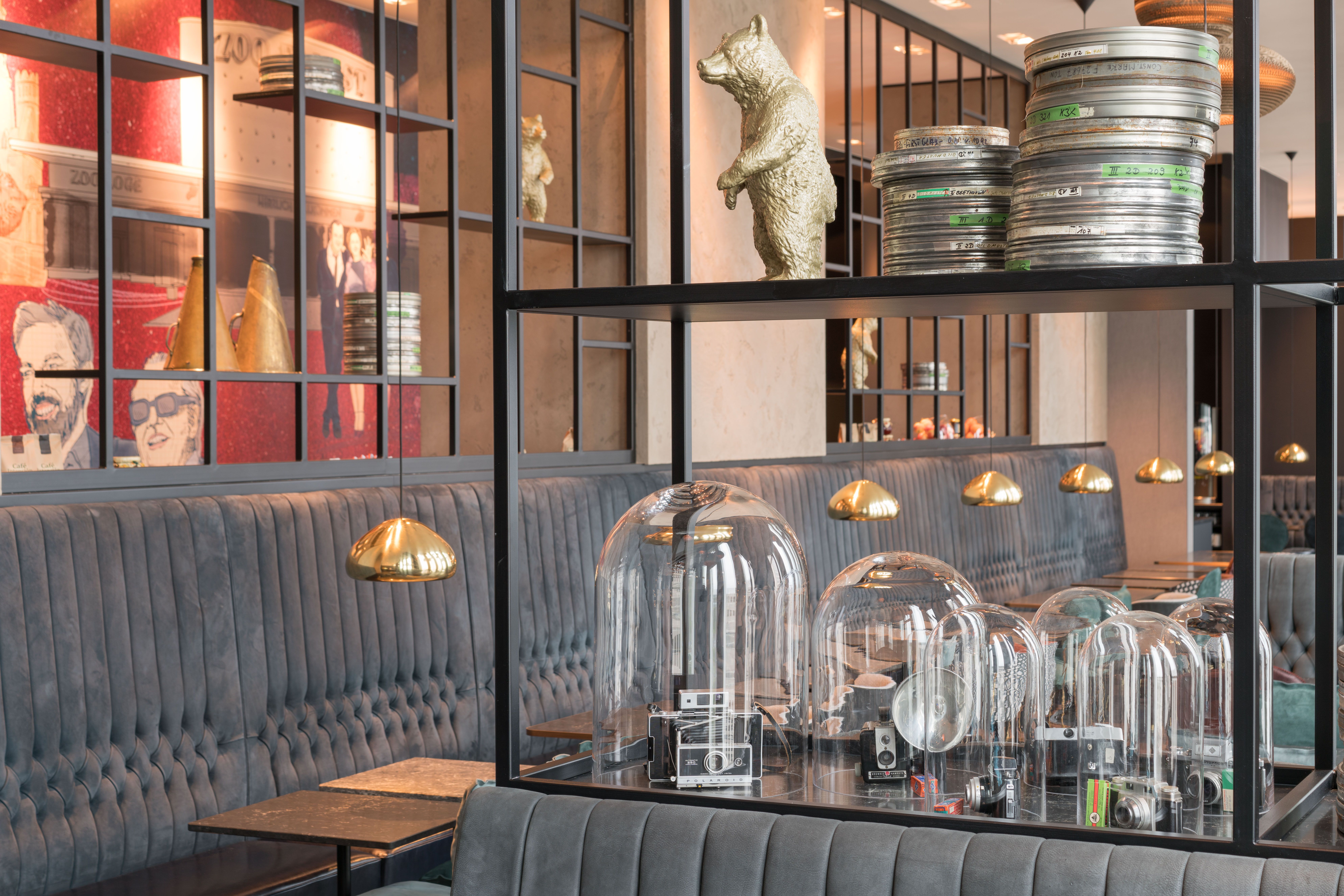 Designhotel Berlin Upper West Motel One helle Lounge mit Tischen und Stühlen sowie ein offenes Regal im Vordergrund mit mehreren Dekorationselementen passend zu dem Motto Berlinale