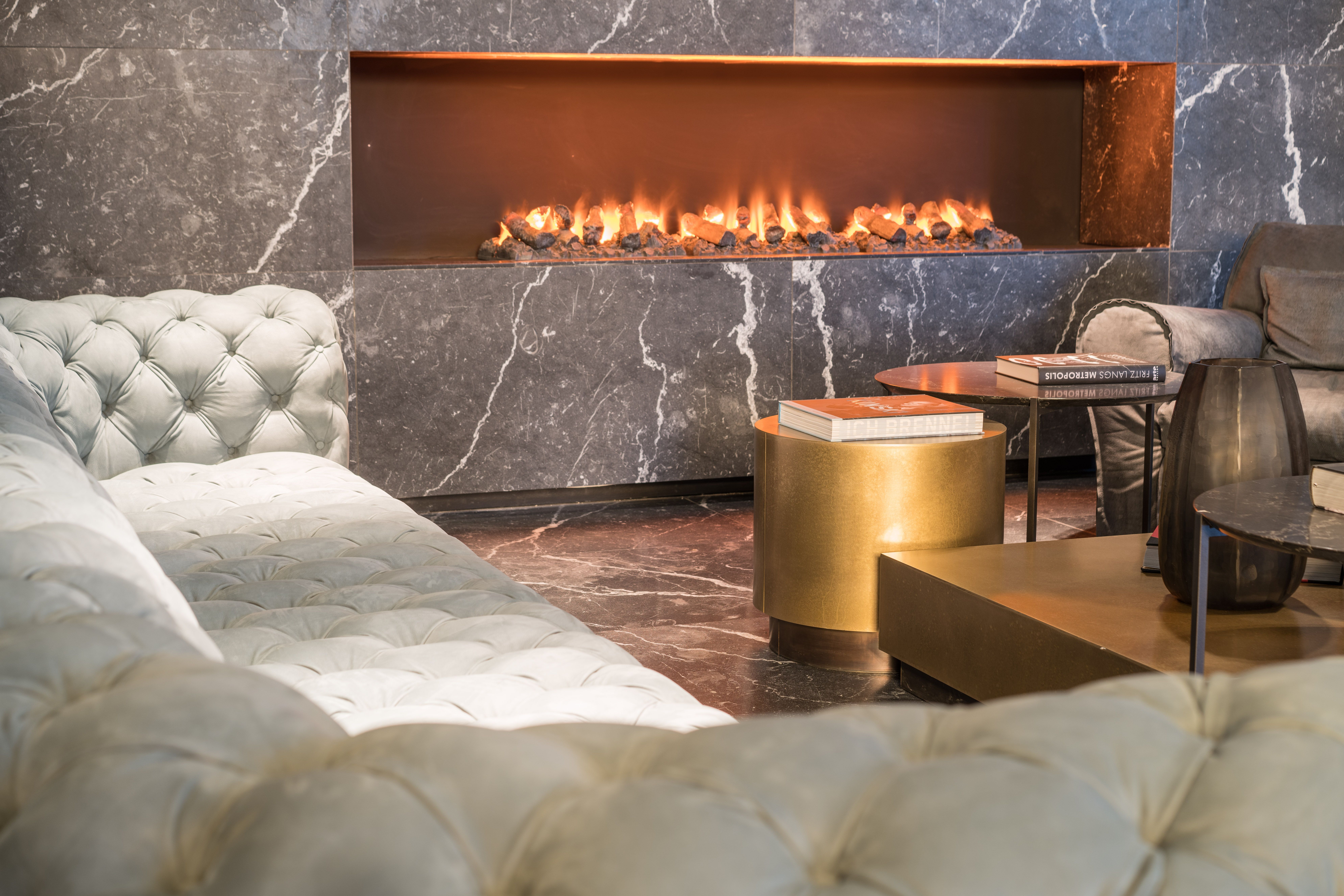 Designhotel Berlin Upper West Motel One Lounge mit Blick auf eine gemütliche Sitzecke mit Sofas und Sesseln sowie ein offener Kamin in der Wand