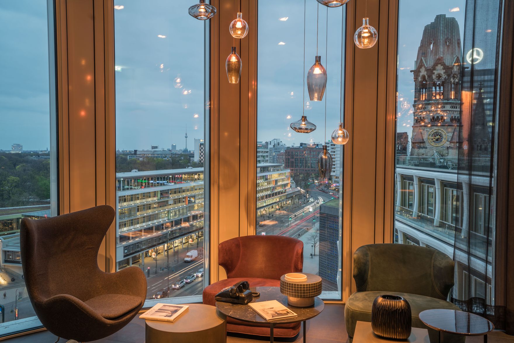 Designhotel Berlin Upper West Motel One Lounge mit Sesseln vor bodentiefen Fenstern und Blick auf die Dächer der Stadt