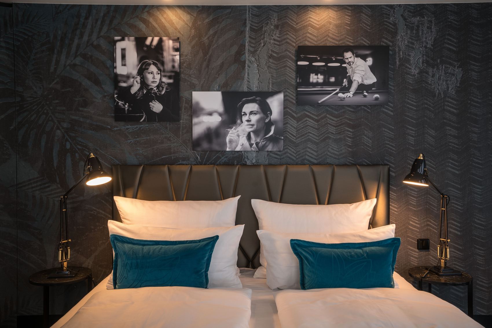 Designhotel Berlin Upper West Motel One Zimmer mit Blick auf ein Doppelbett mit Zierkissen in türkis sowie drei Bilder in schwarz-weiß von Schauspielern an der Wand