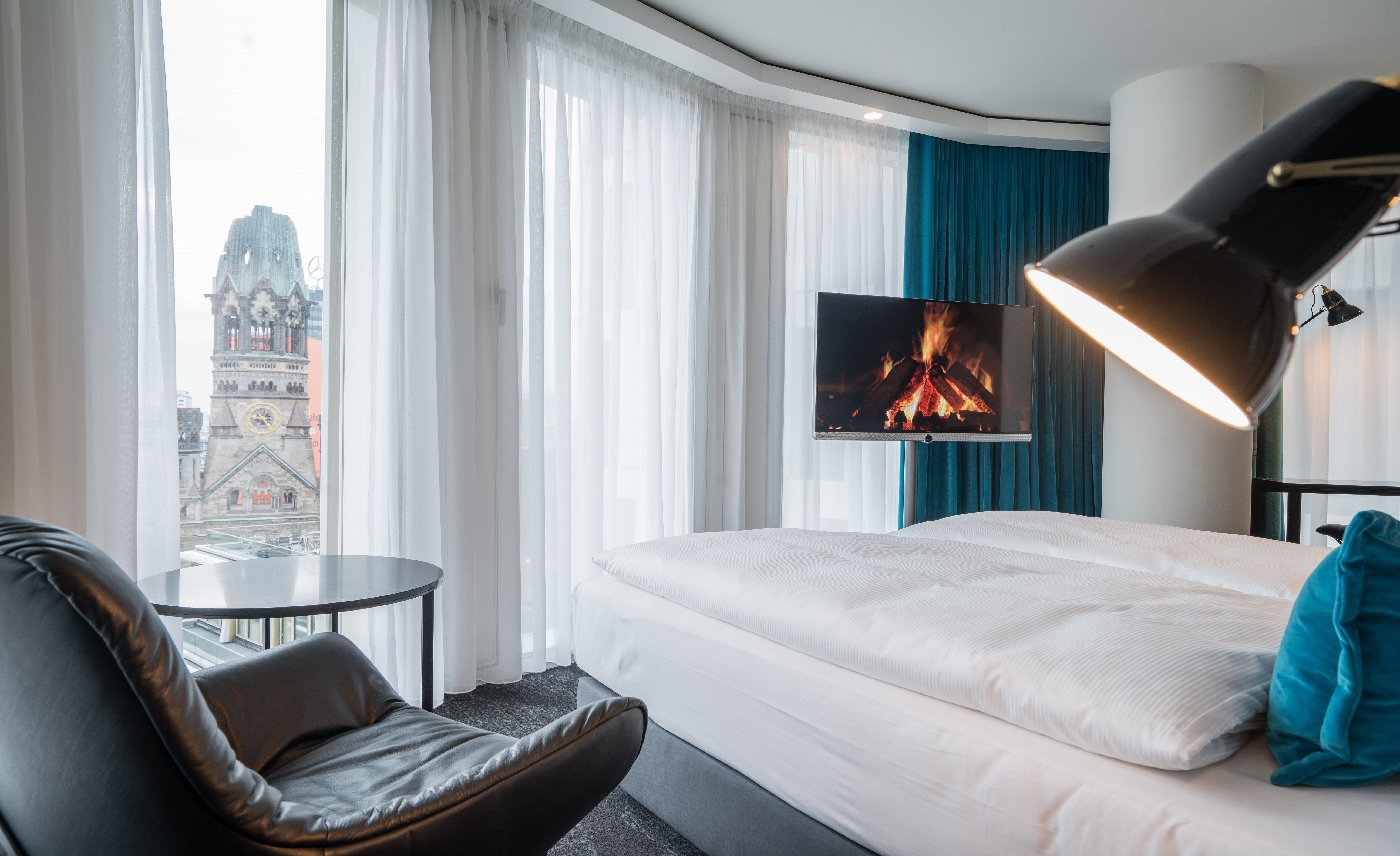 Designhotel Berlin Upper West Motel One helles Zimmer mit großer Fensterfront, komfortablem Doppelbett, Fernseher sowie ein Sessel mit Beistelltisch