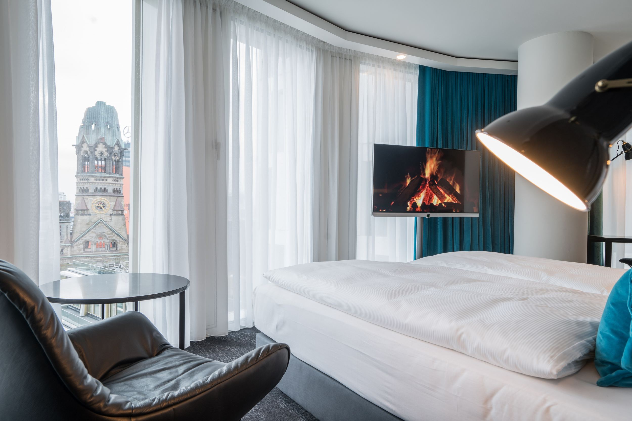 Designhotel Berlin Upper West Motel One helles Zimmer mit großer Fensterfront, komfortablem Doppelbett, Fernseher sowie ein Sessel mit Beistelltisch