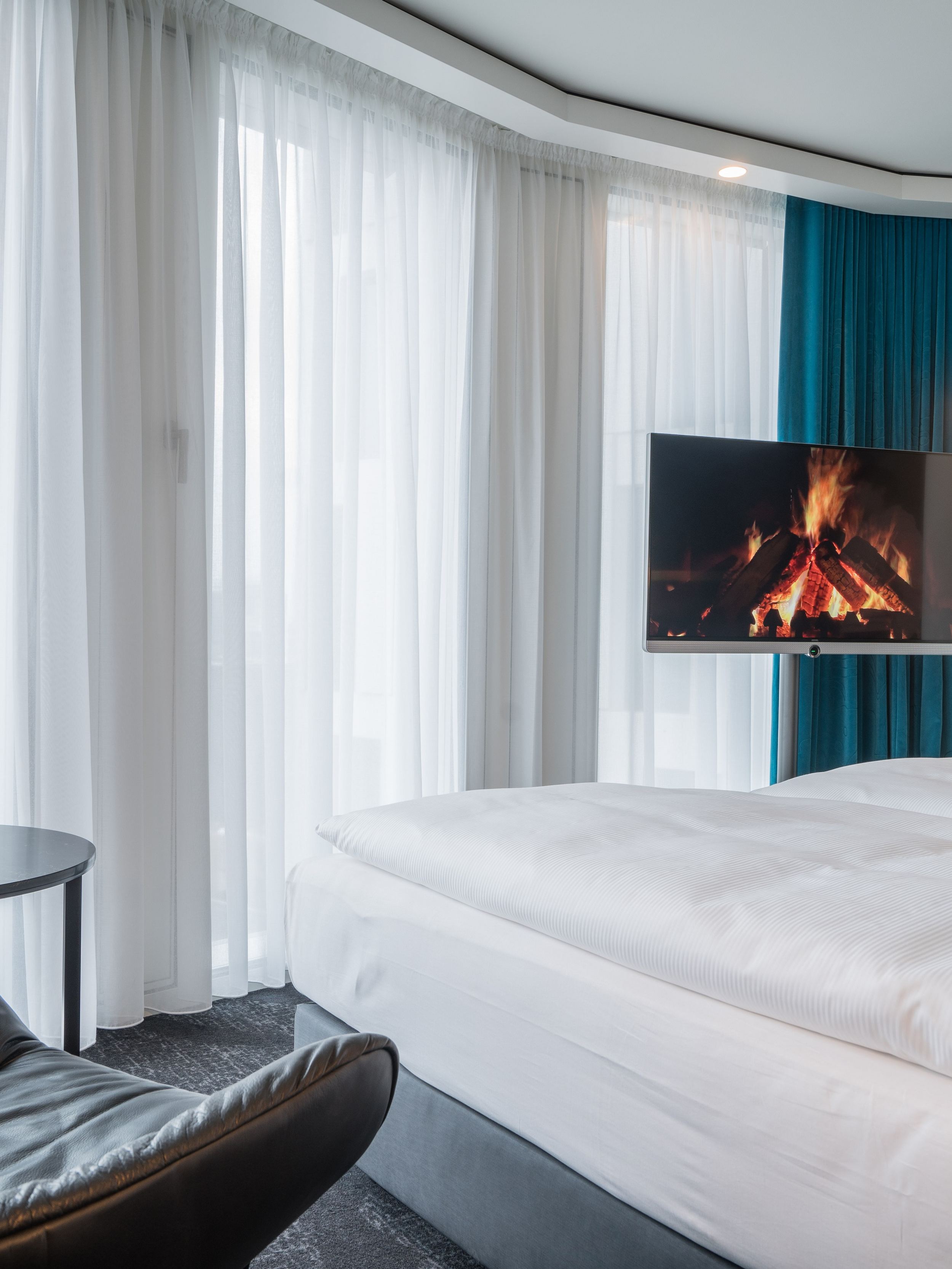 Designhotel Berlin Upper West Motel One helles Zimmer mit großer Fensterfront, komfortablem Doppelbett, Fernseher sowie ein Sessel mit Beistelltisch