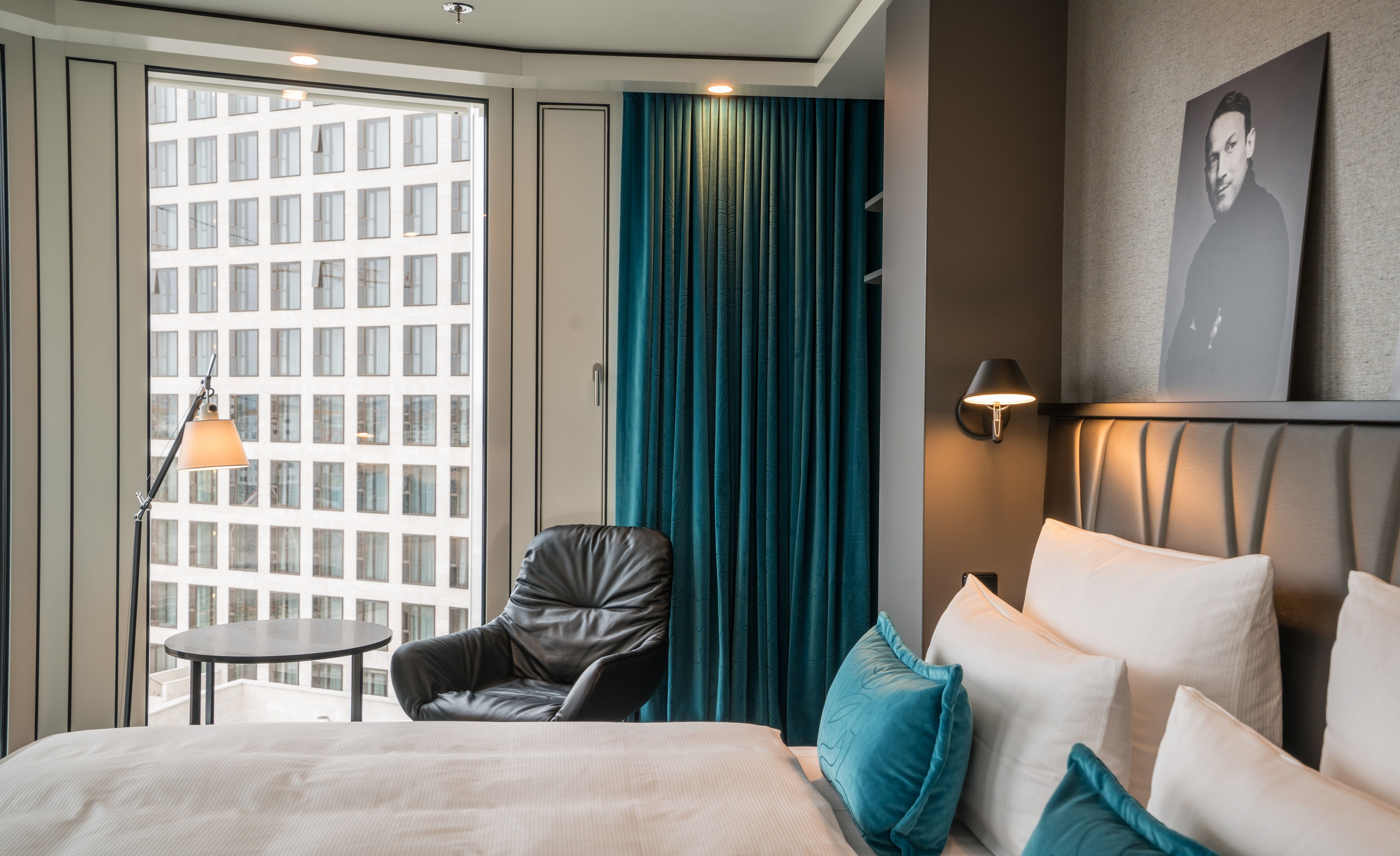 Designhotel Berlin Upper West Motel One lichtdurchflutetes Doppelzimmer mit geräumigem Bett sowie einem Sessel mit Beistelltisch und Stehlampe vor einem großen Fenster