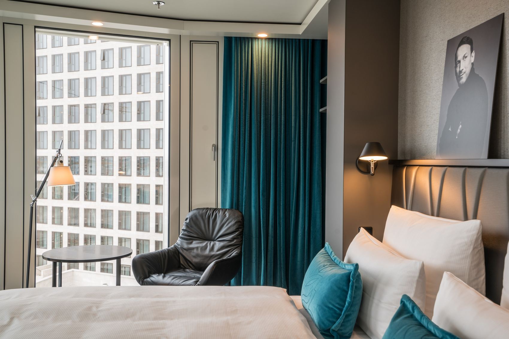Designhotel Berlin Upper West Motel One lichtdurchflutetes Doppelzimmer mit geräumigem Bett sowie einem Sessel mit Beistelltisch und Stehlampe vor einem großen Fenster