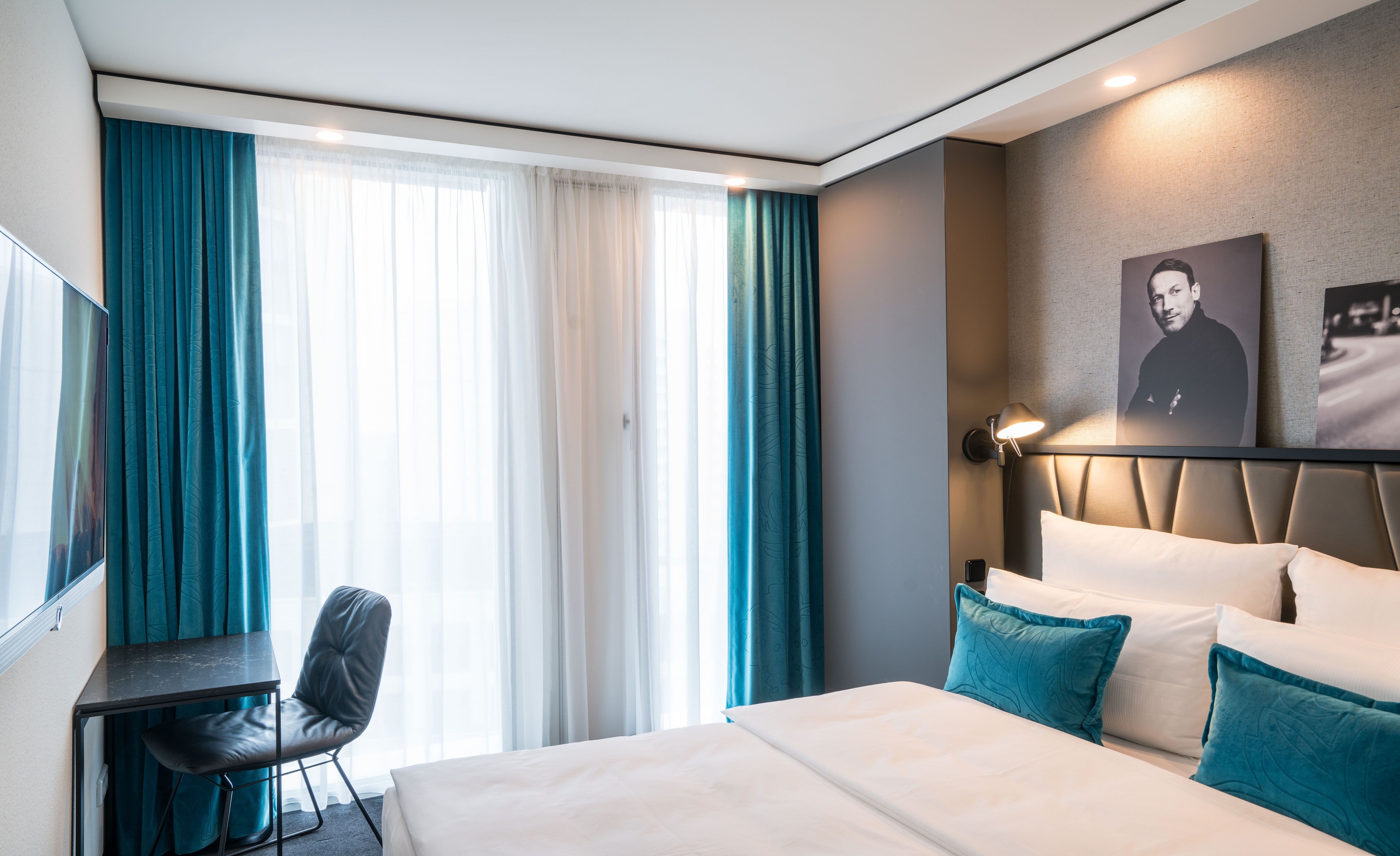 Designhotel Berlin Upper West Motel One helles Doppelzimmer mit bodentiefen Fenstern sowie Doppelbett, Tisch, Stuhl und Fernseher an der Wand