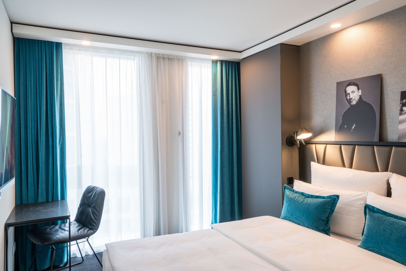 Designhotel Berlin Upper West Motel One helles Doppelzimmer mit bodentiefen Fenstern sowie Doppelbett, Tisch, Stuhl und Fernseher an der Wand